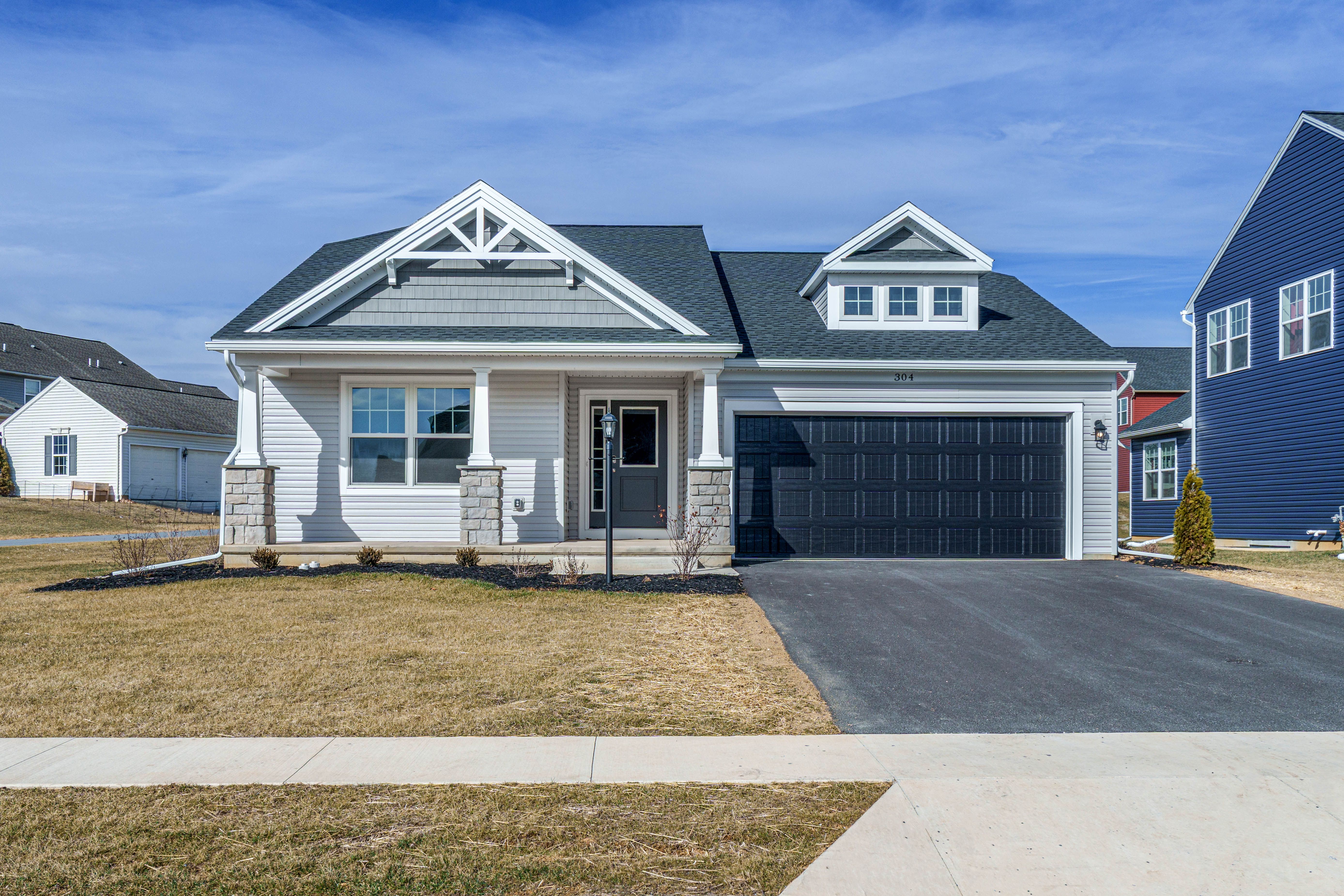 Front view of a single-story home with light siding, stone accents, covered porch, black garage door, and paved driveway