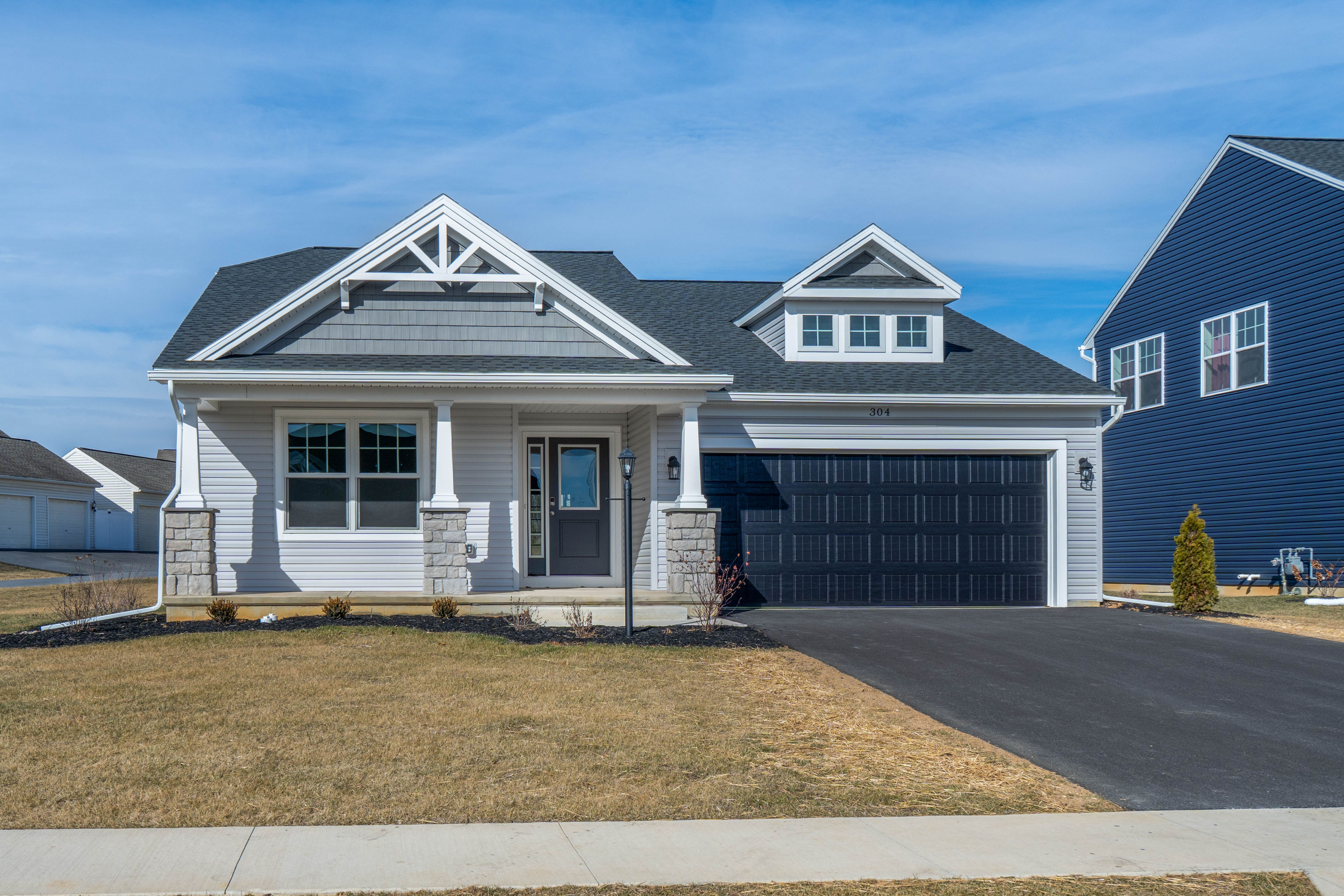 Straight-on view of the homes front elevation featuring a covered porch, stone columns, and dark garage door