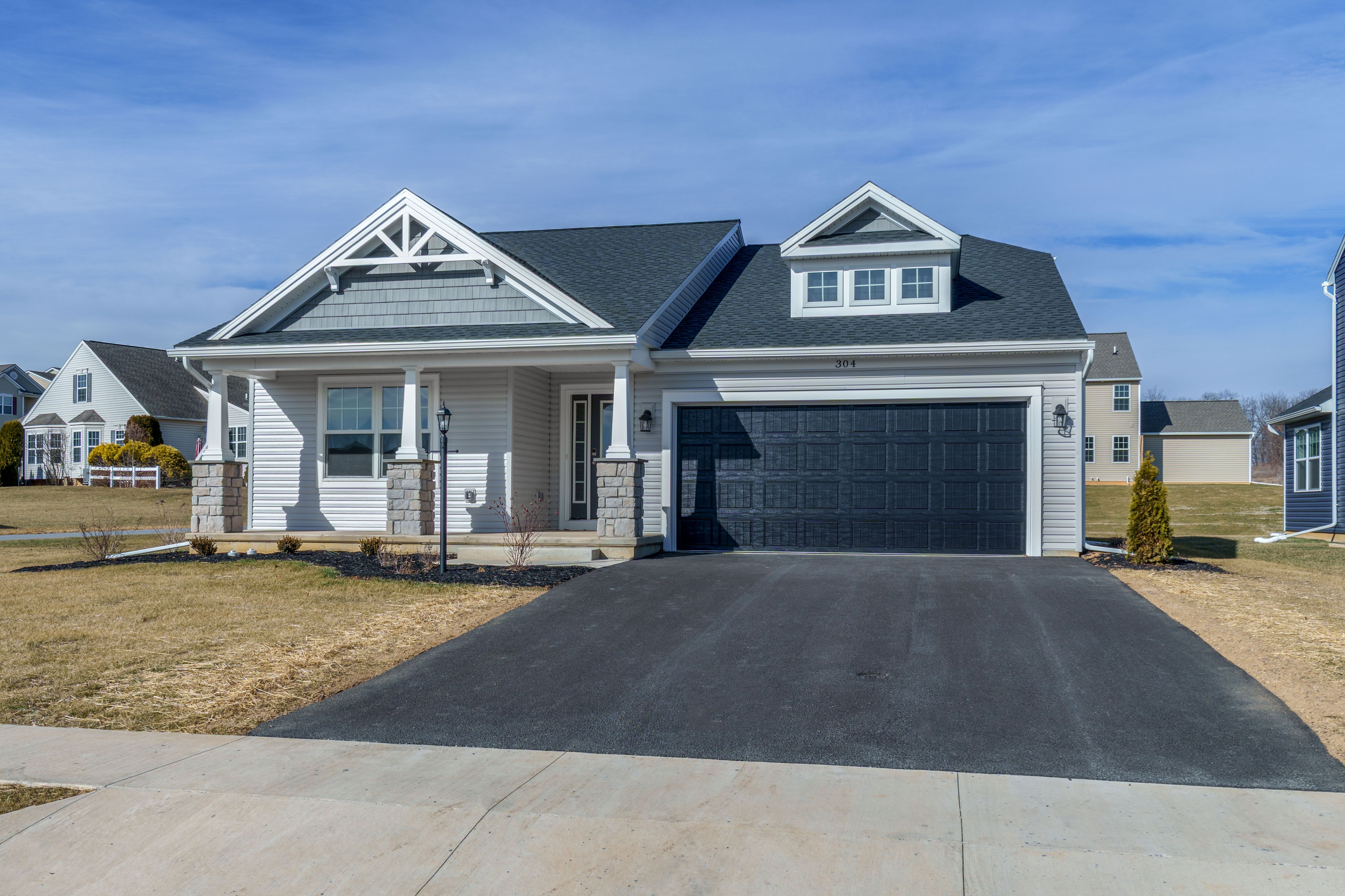 Angled front exterior showing gabled rooflines, covered porch with stone columns, and attached two-car garage