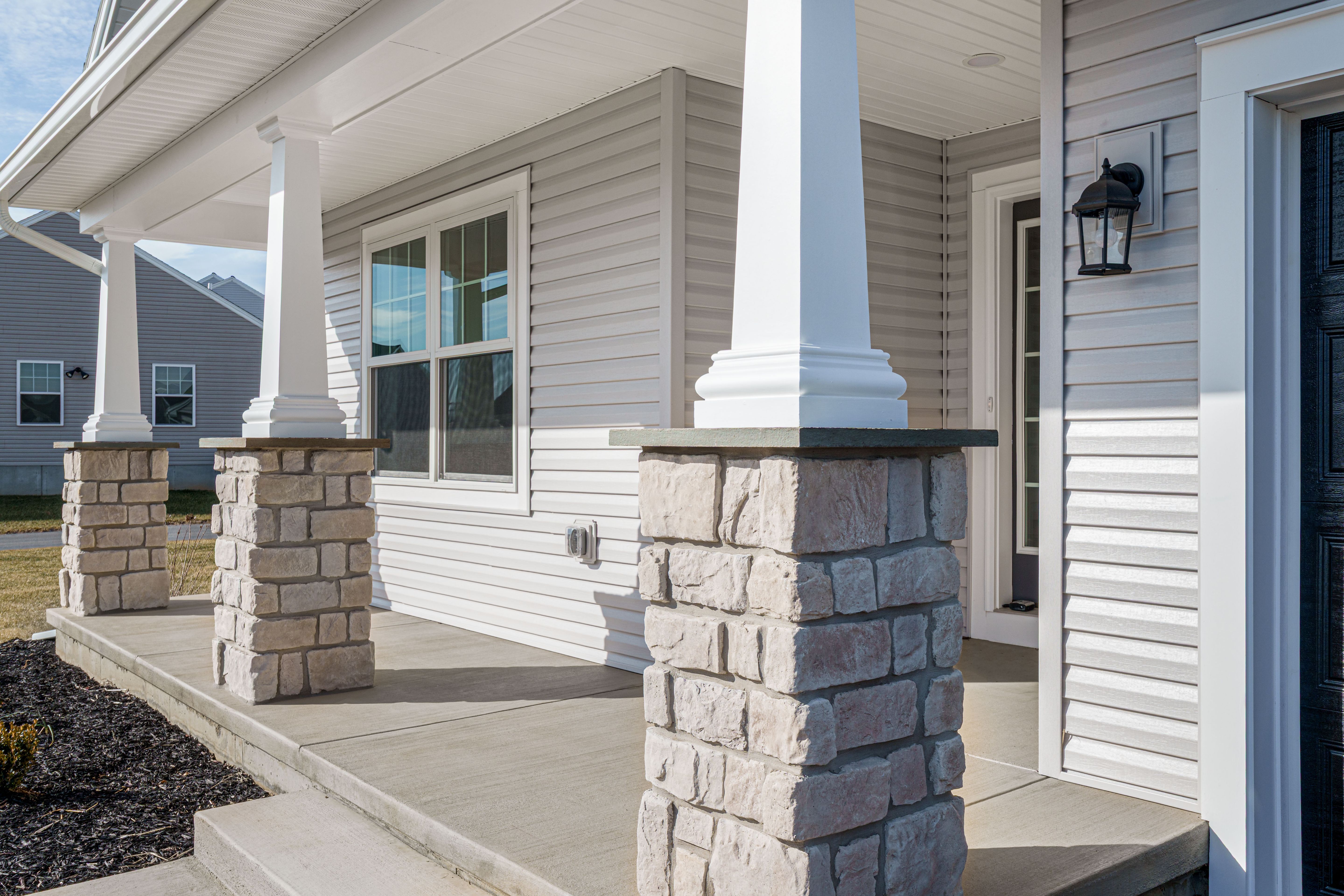 Close-up of the covered front porch with white columns, stone bases, concrete floor, and front entry door
