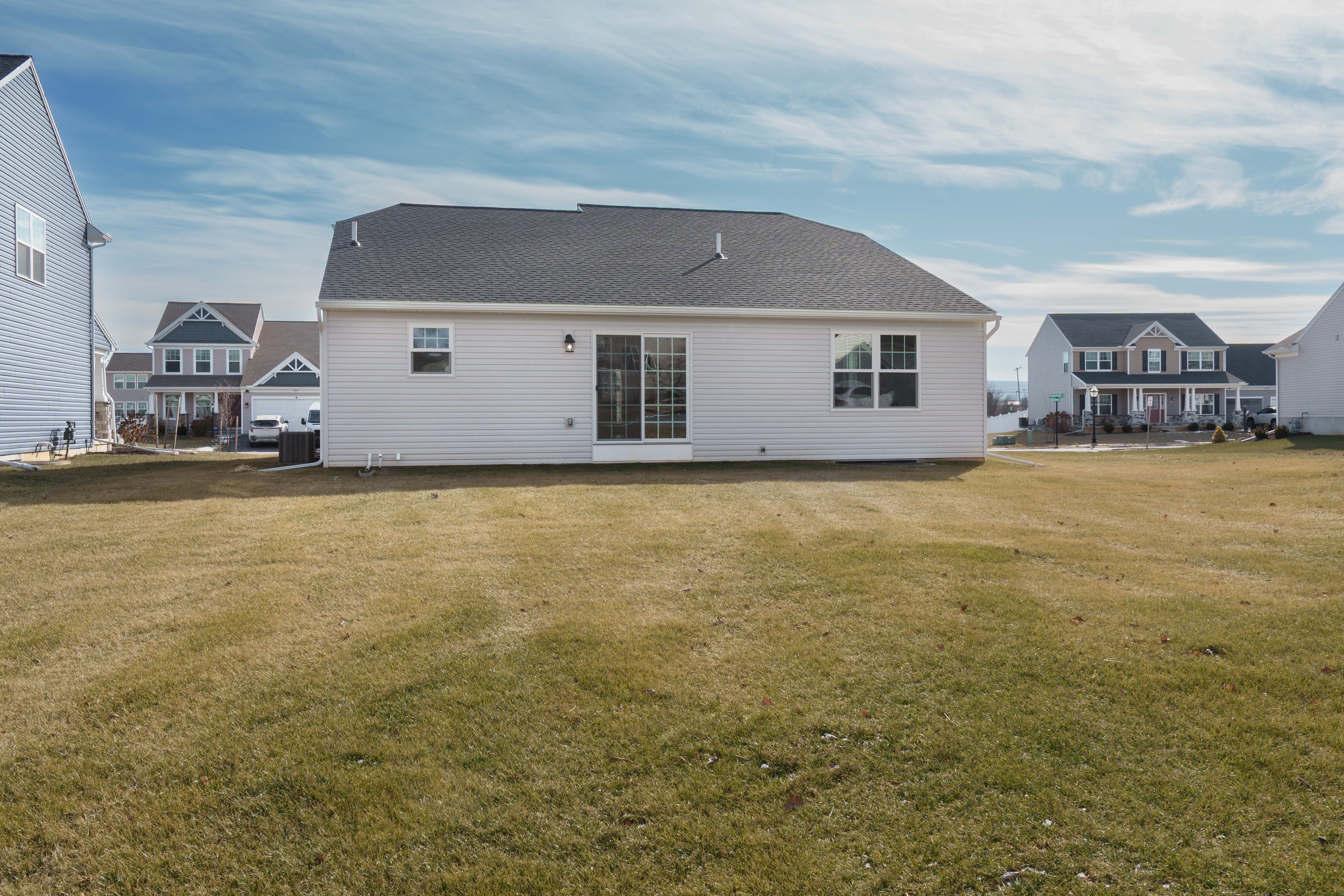 Wide rear view showing sliding glass door, multiple windows, open backyard space, and surrounding neighborhood