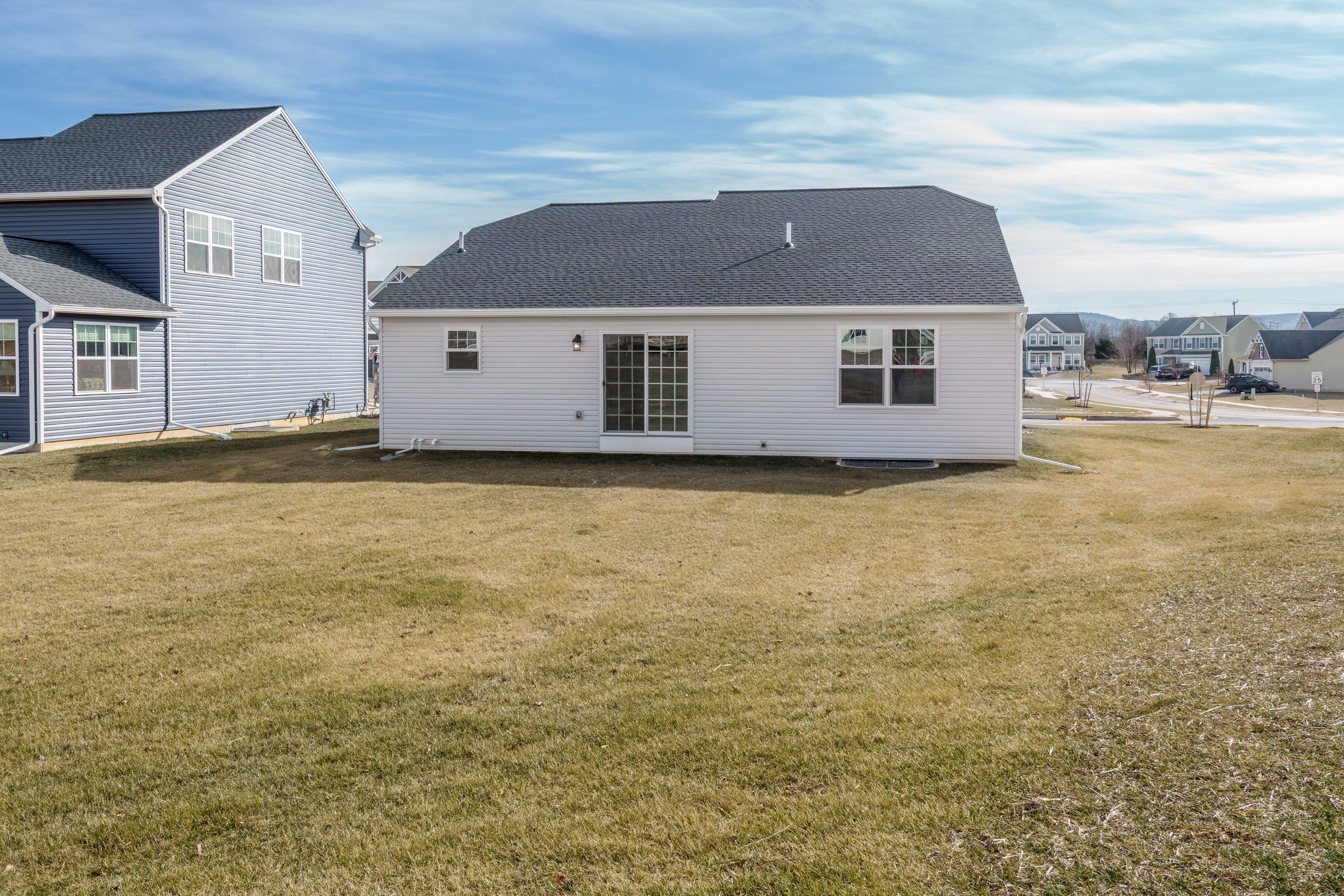 Rear exterior of the home with light siding, sliding glass door, backyard lawn, and neighboring homes visible