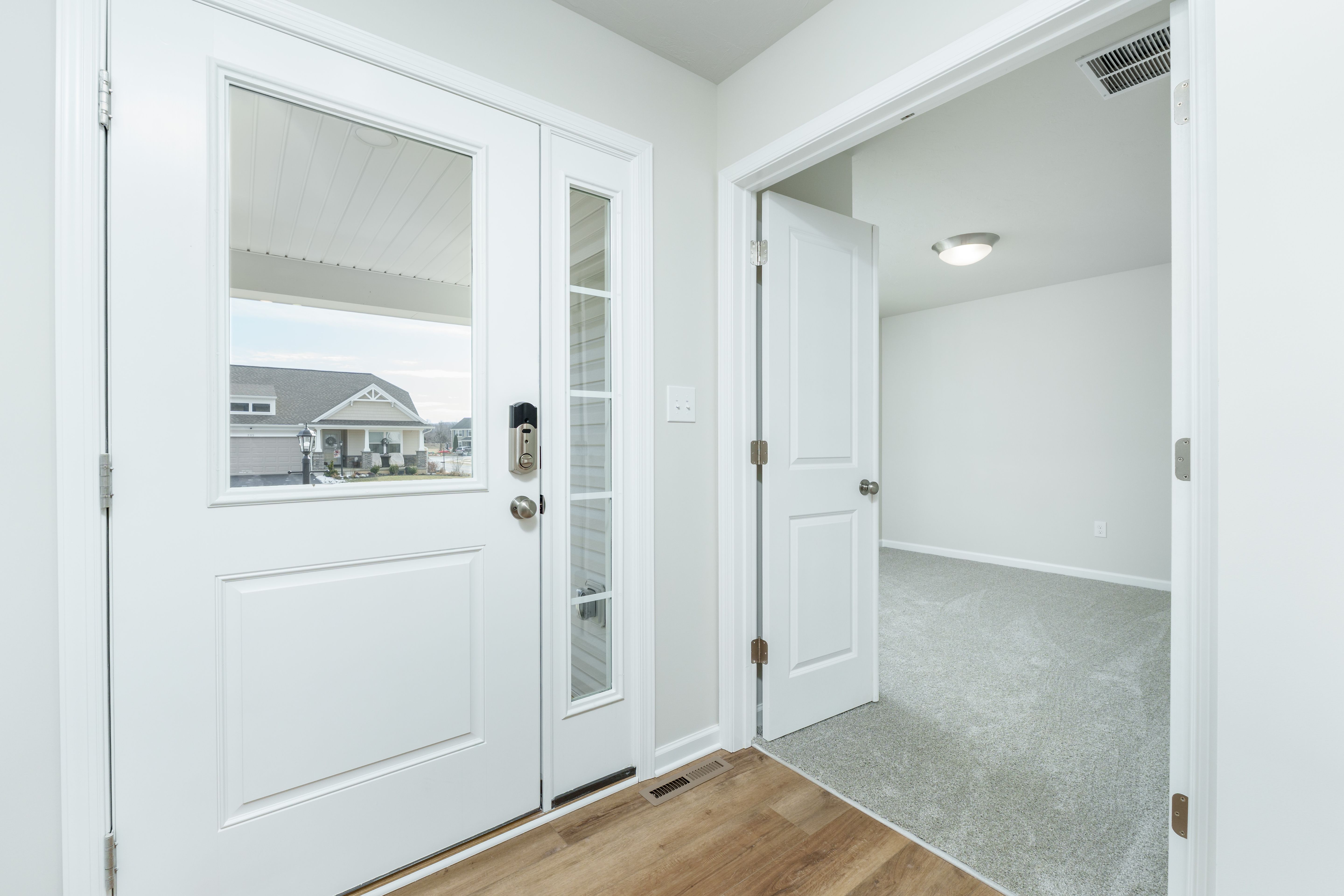Entry foyer showing front door with glass panel, luxury vinyl plank flooring, and adjacent bedroom doorway