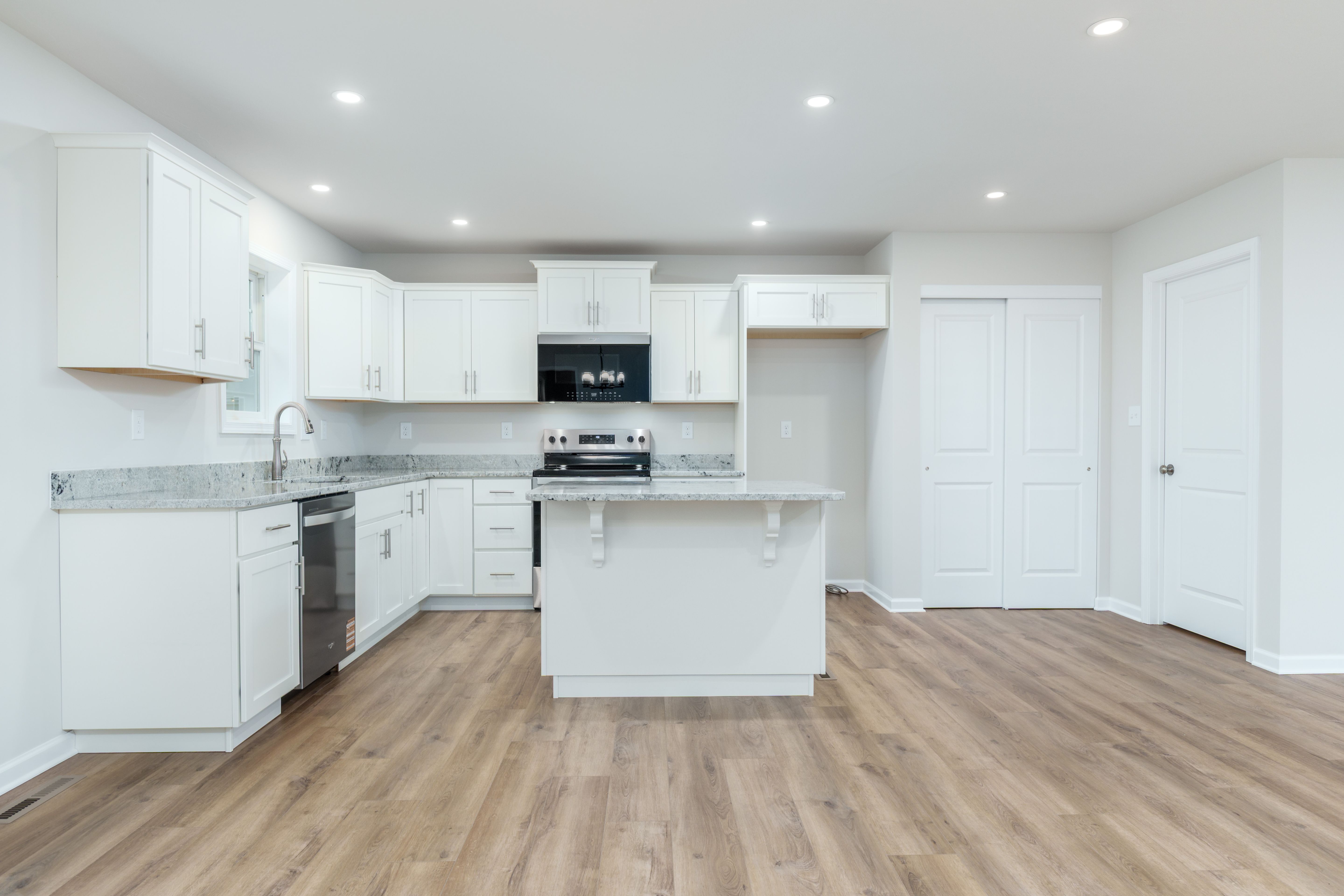 Wide kitchen view featuring island seating, white cabinets, pantry doors, and luxury vinyl plank flooring