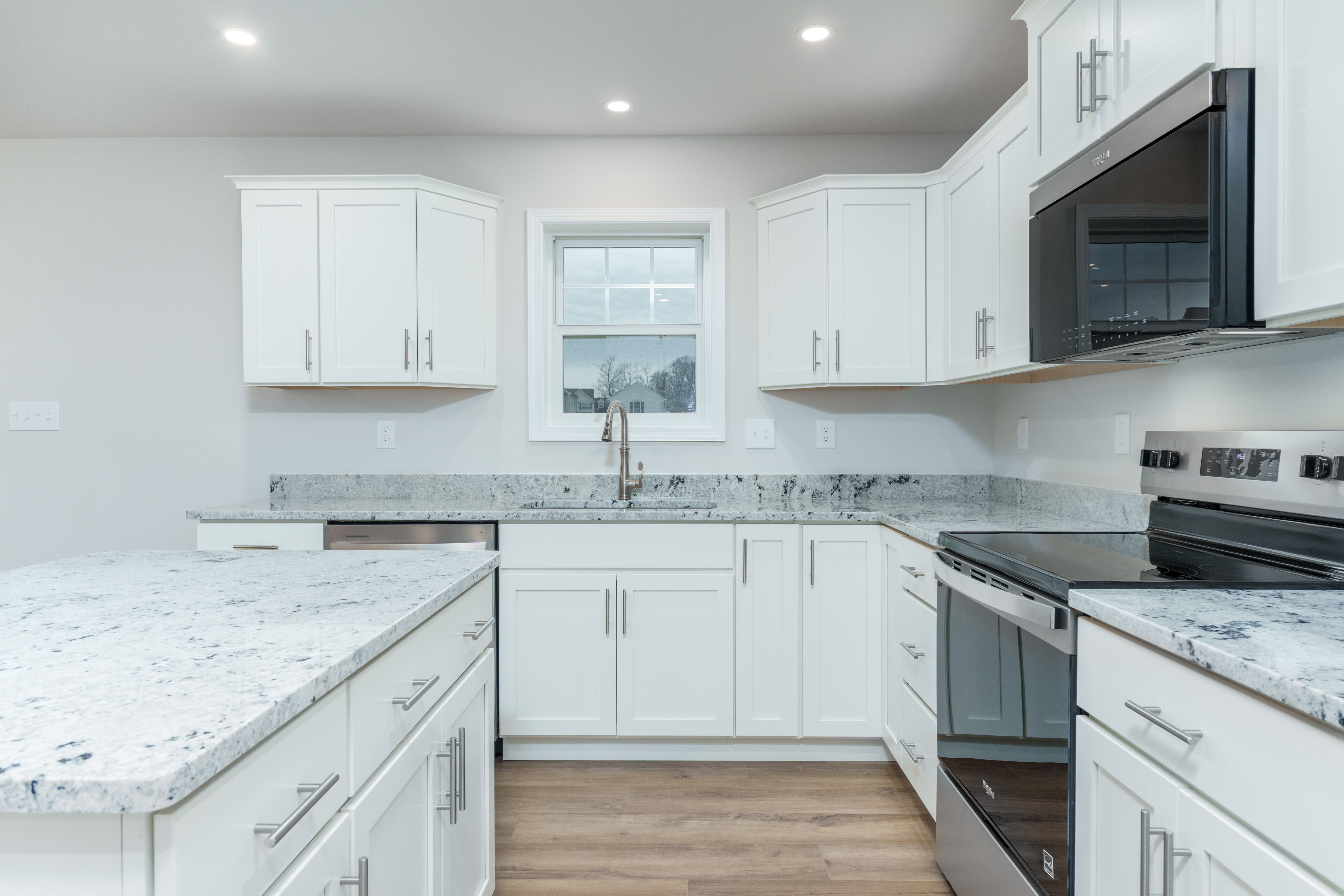 Kitchen workspace with sink under window, granite-style counters, stainless range, and white cabinetry