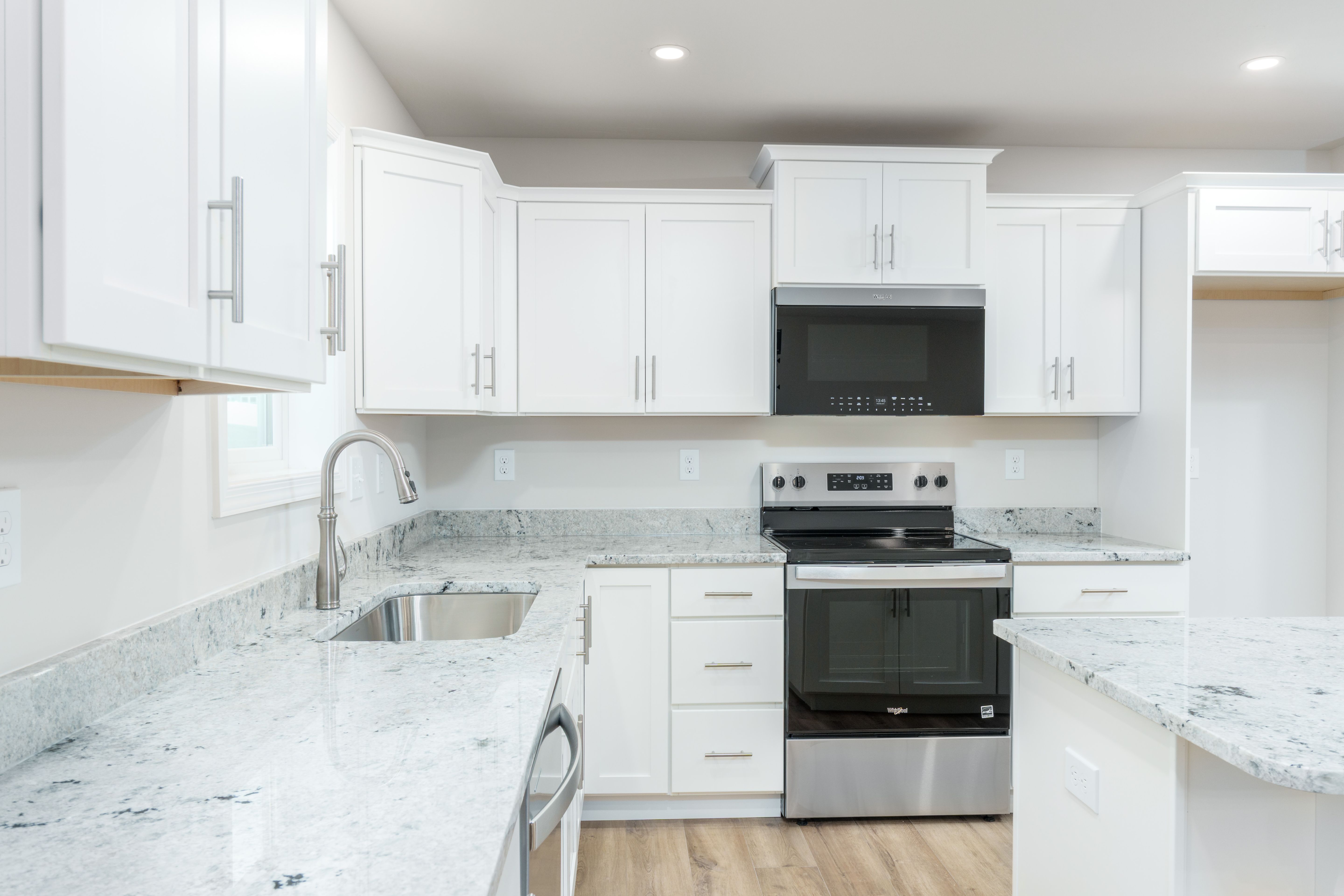 Close-up of kitchen counters, sink, stainless range, white cabinets, and modern finishes