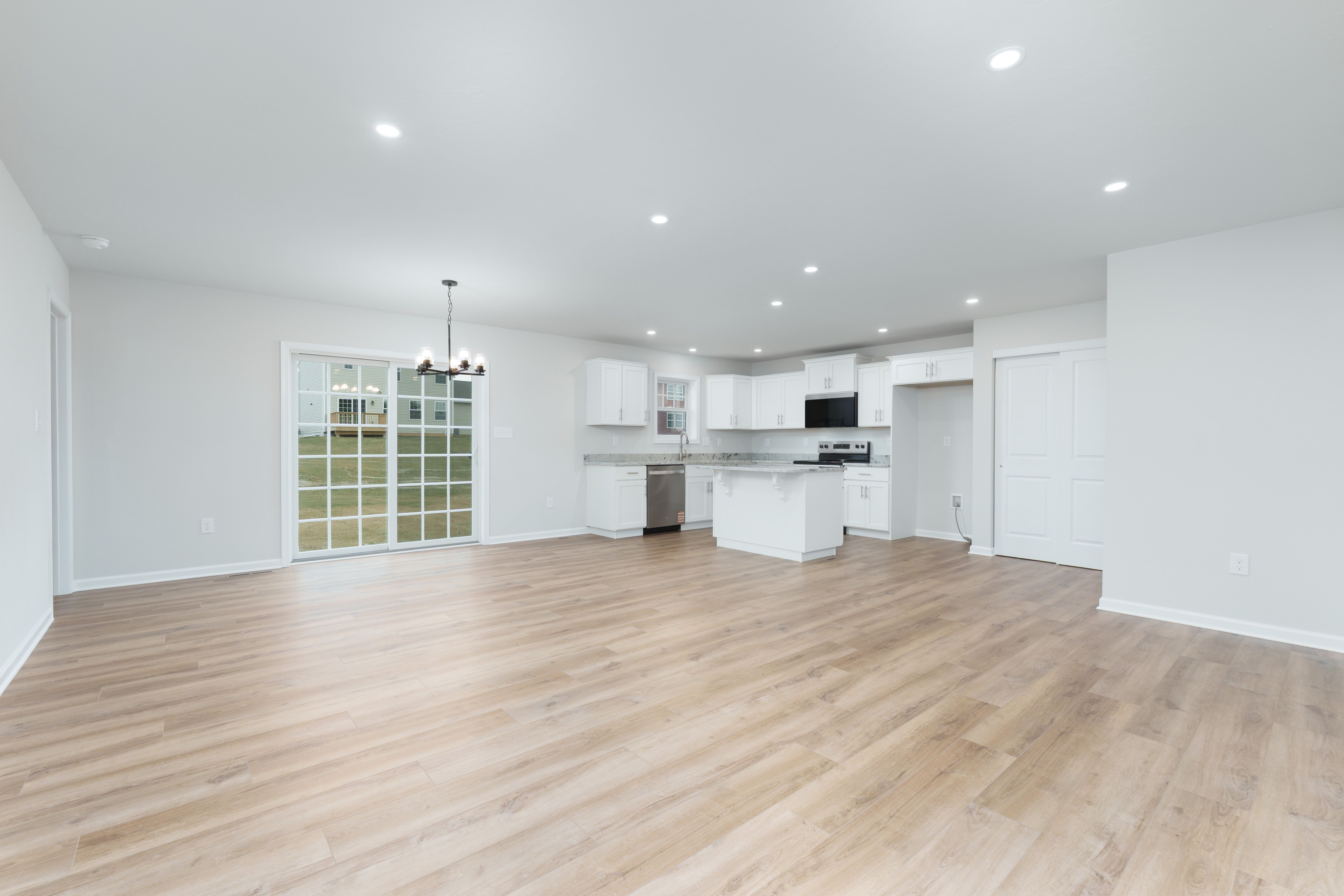 Open-concept living area with luxury vinyl plank flooring, recessed lighting, sliding glass door, and bright white kitchen
