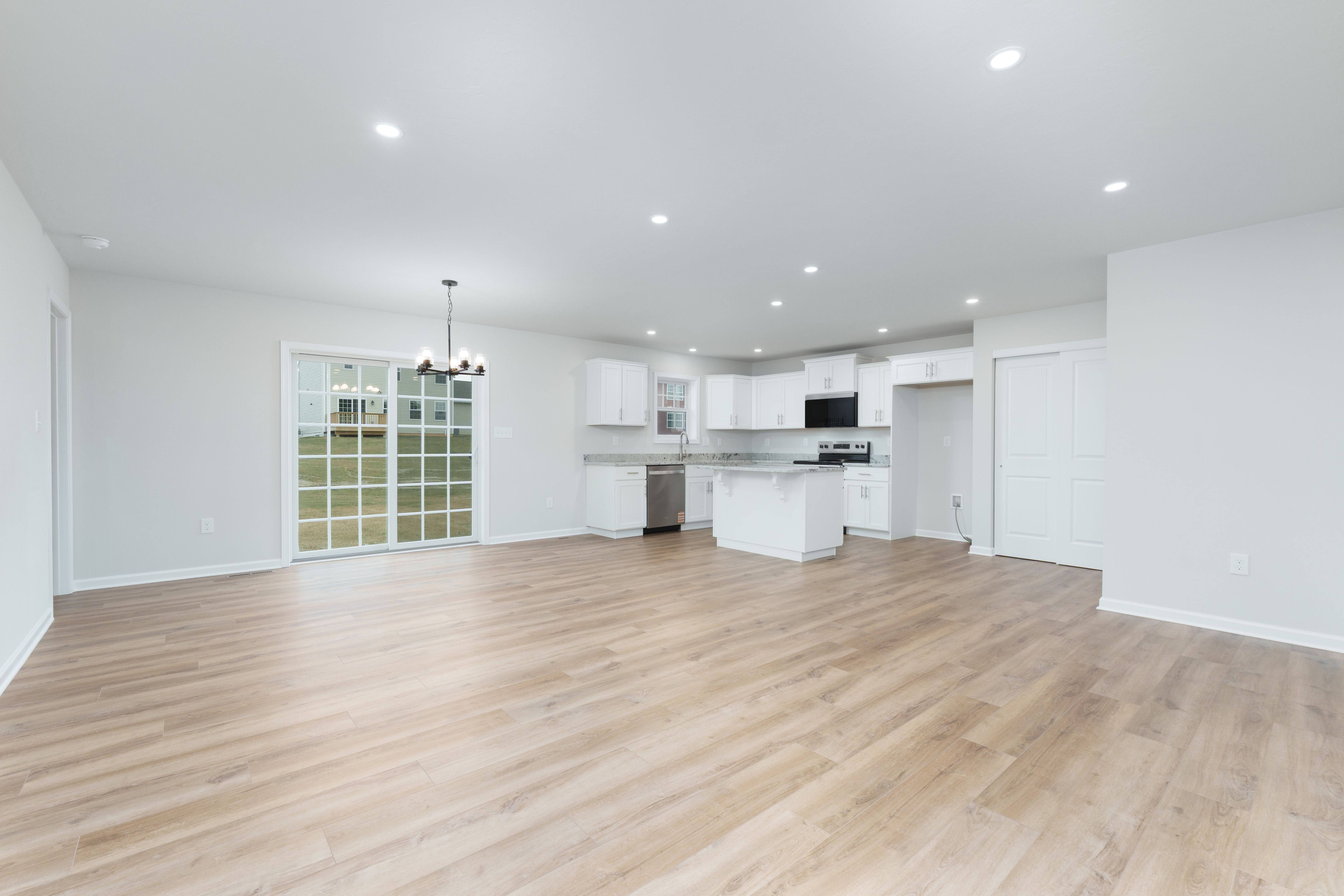 Open-concept living area with luxury vinyl plank flooring, recessed lighting, sliding glass door, and bright white kitchen
