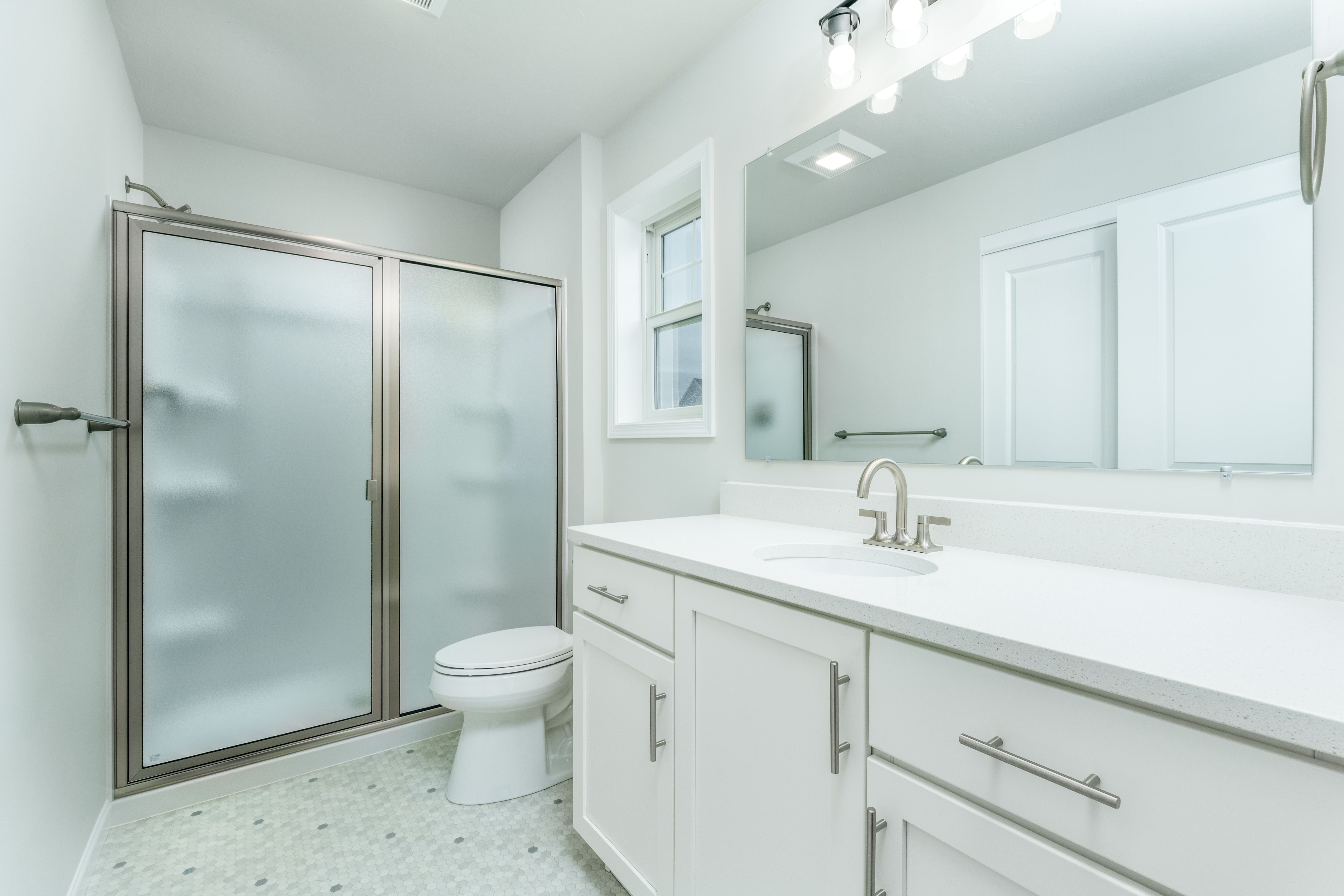 Owners bathroom with dual-sink vanity, framed mirror, frosted glass shower, and tile flooring