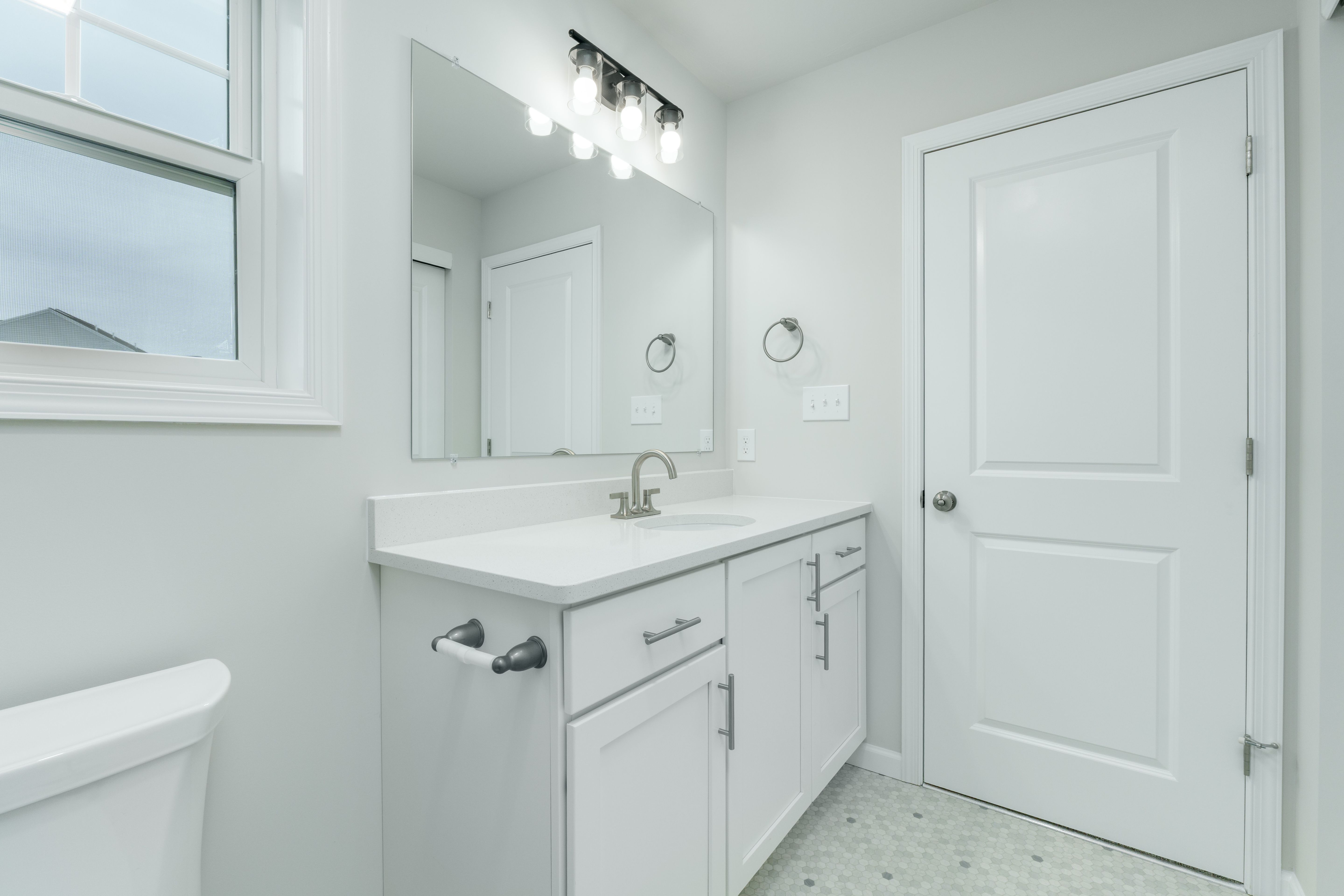 Owners bathroom vanity with modern lighting, white cabinetry, tile floor, and adjacent shower