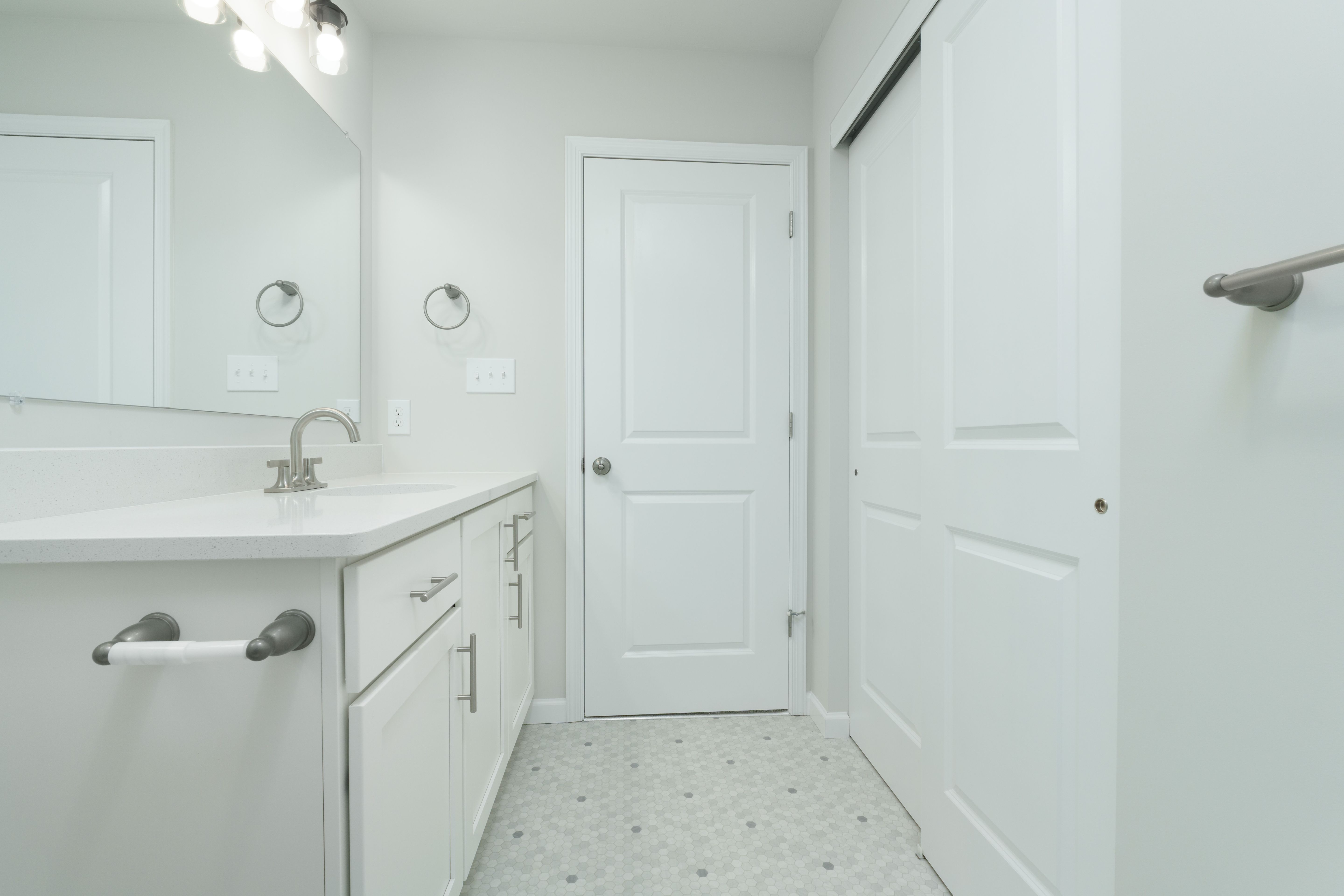 Owners bathroom vanity area with white cabinetry, modern lighting, tile flooring, and nearby closet doors