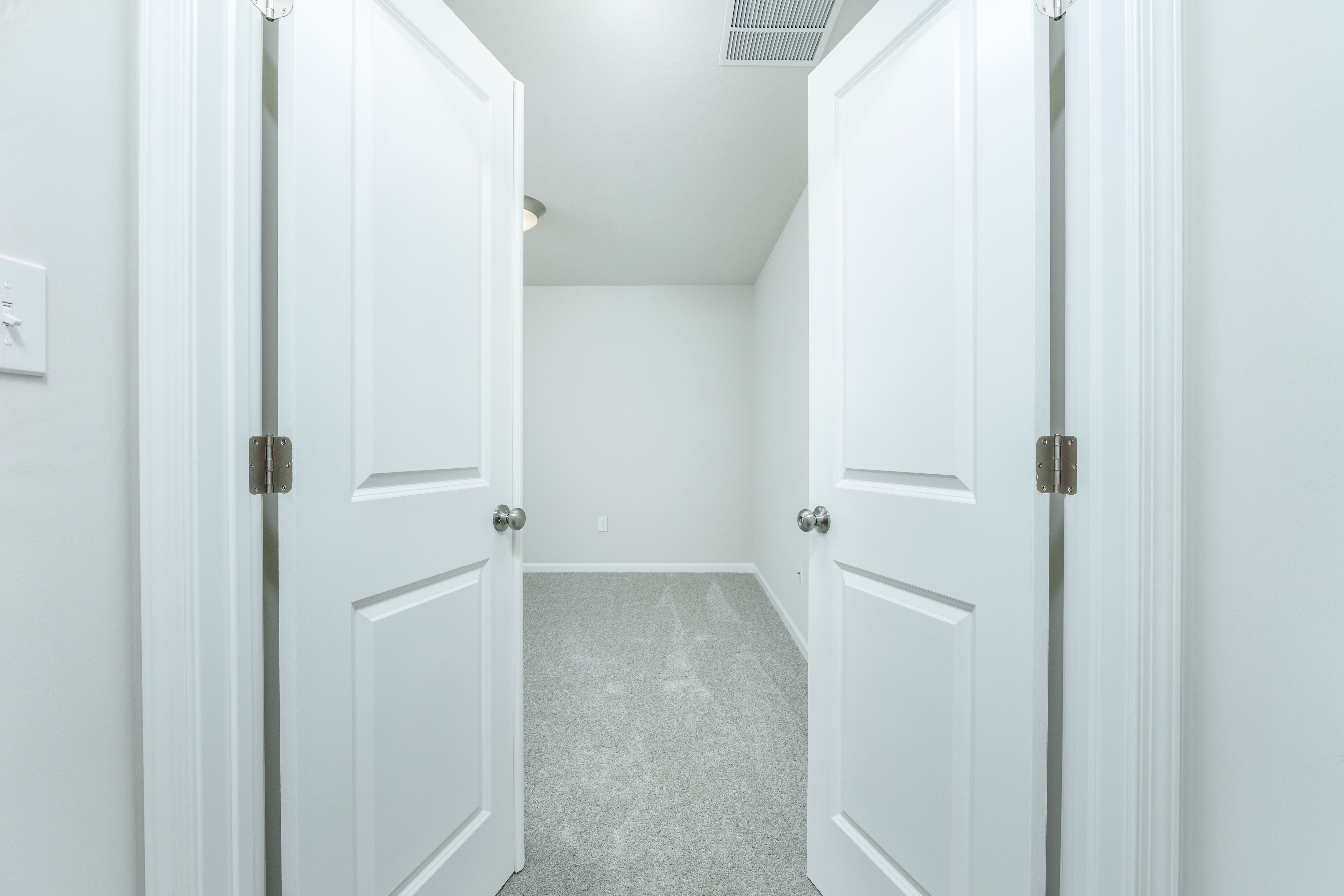 View through double doors into an bedroom with carpeted flooring, neutral walls, and ceiling light