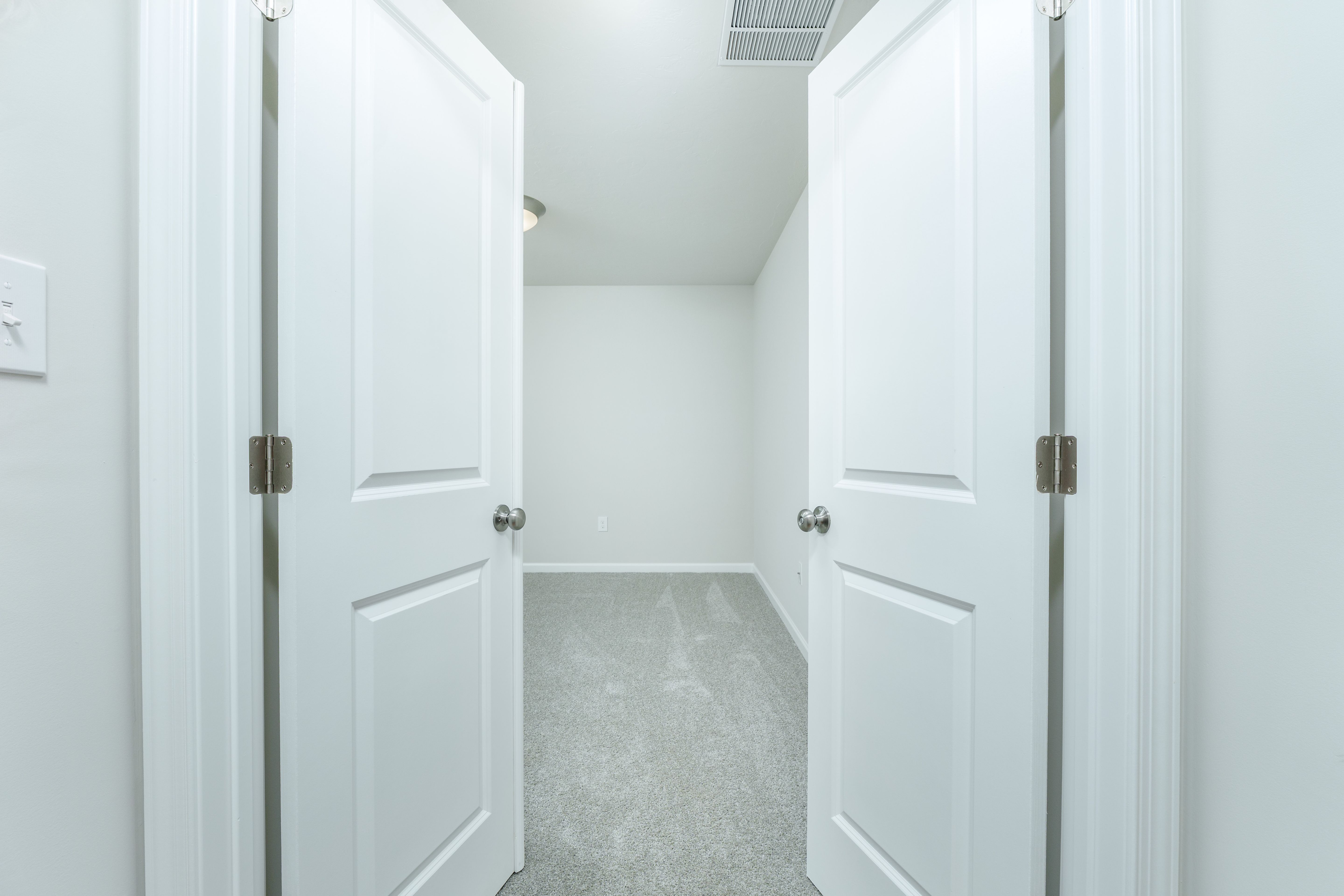 View through double doors into an bedroom with carpeted flooring, neutral walls, and ceiling light