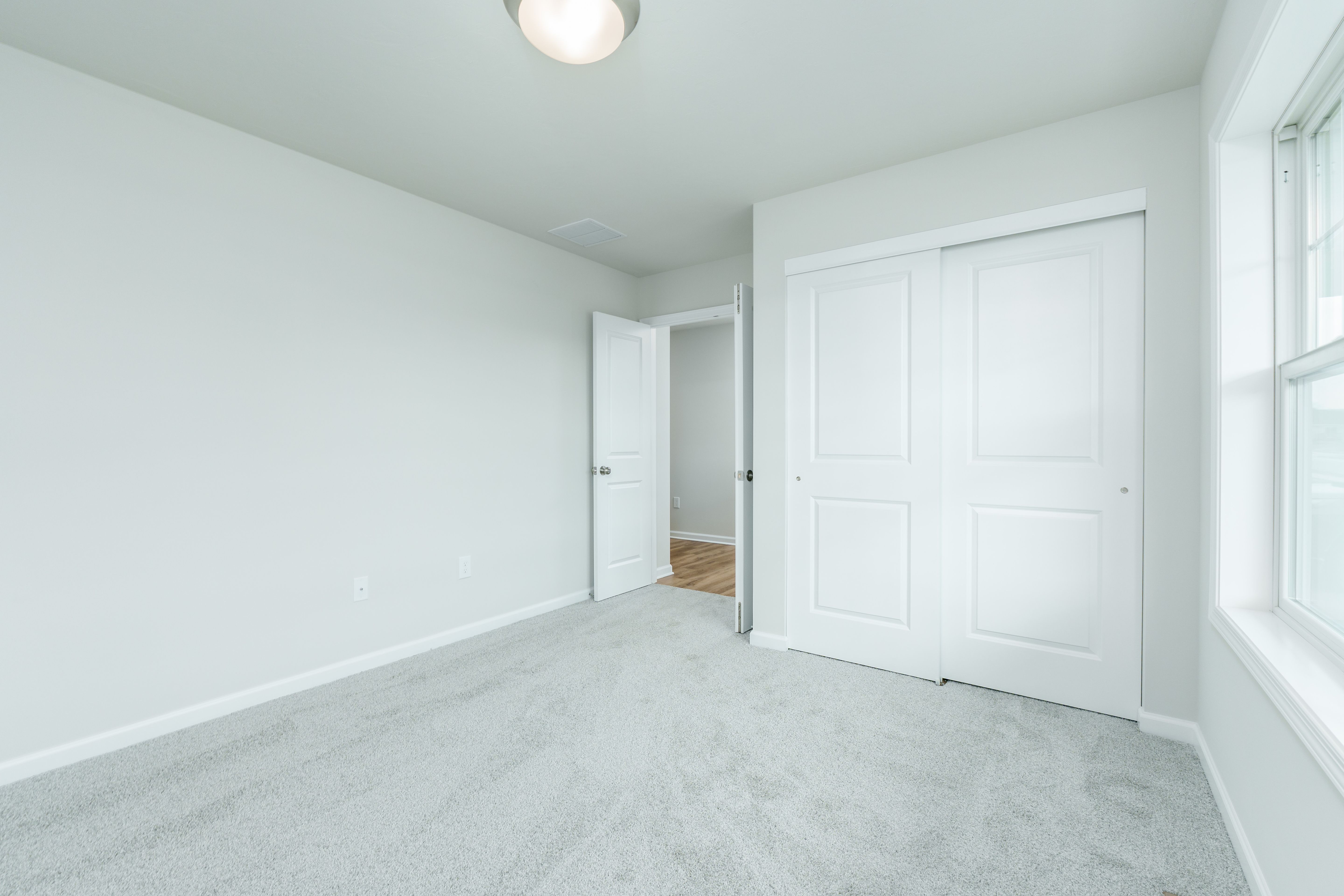 Bedroom featuring carpeted flooring, sliding closet doors, neutral walls, and a nearby hallway entry