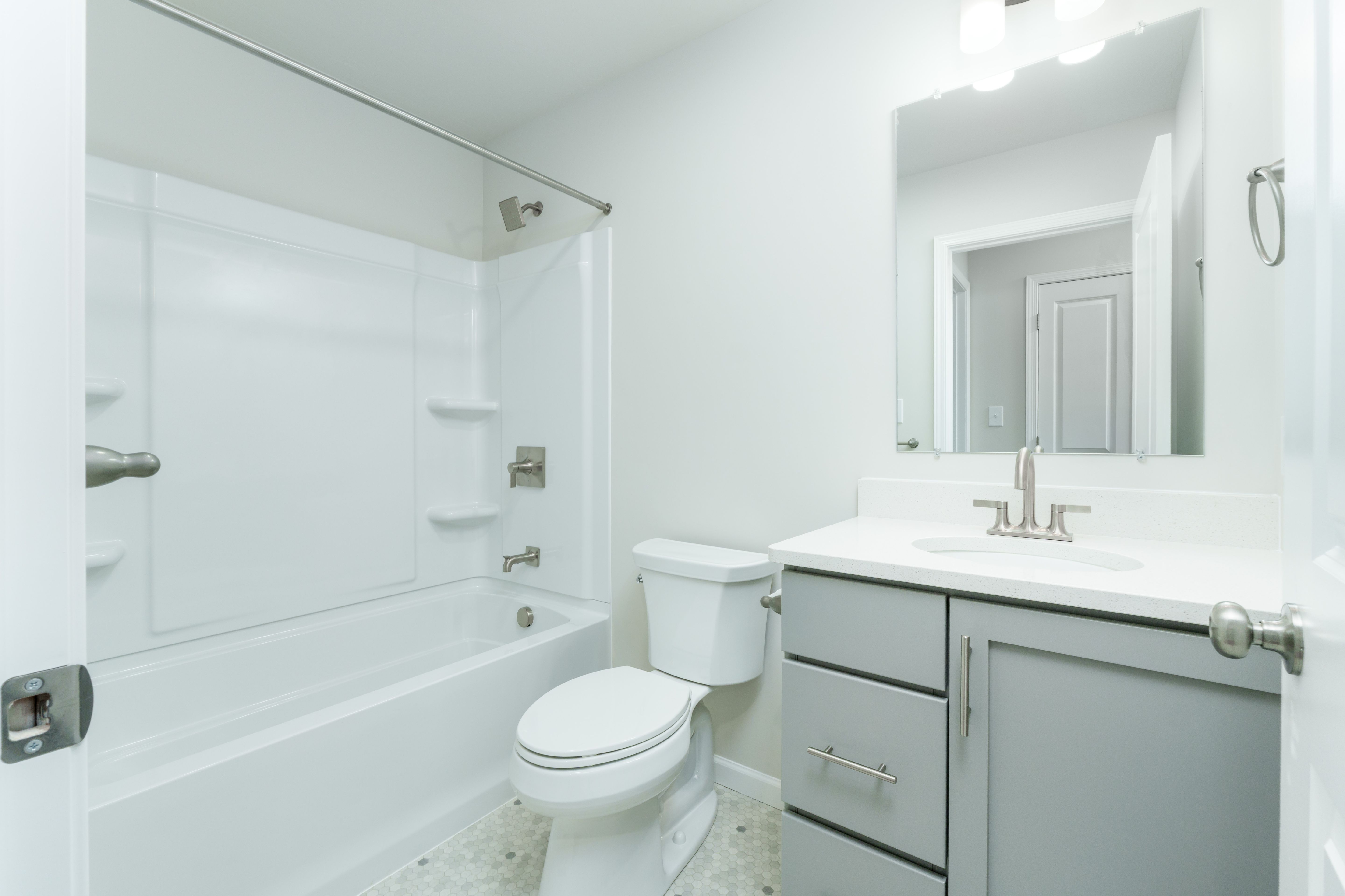 Secondary bathroom with tub and shower combo, white surround, toilet, gray vanity, and bright overhead lighting