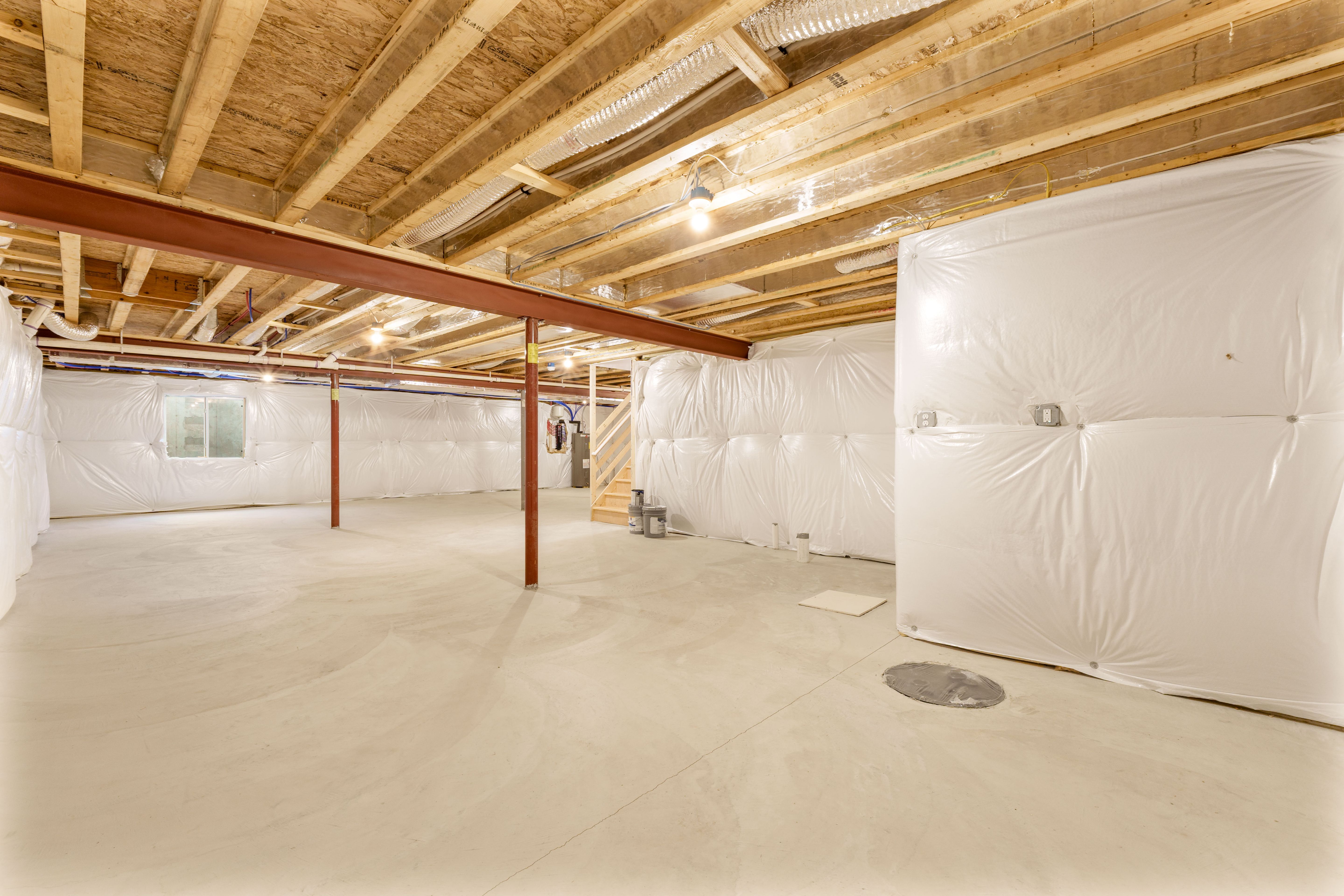 Wide view of an unfinished basement with concrete floor, exposed beams, support columns, and insulated walls