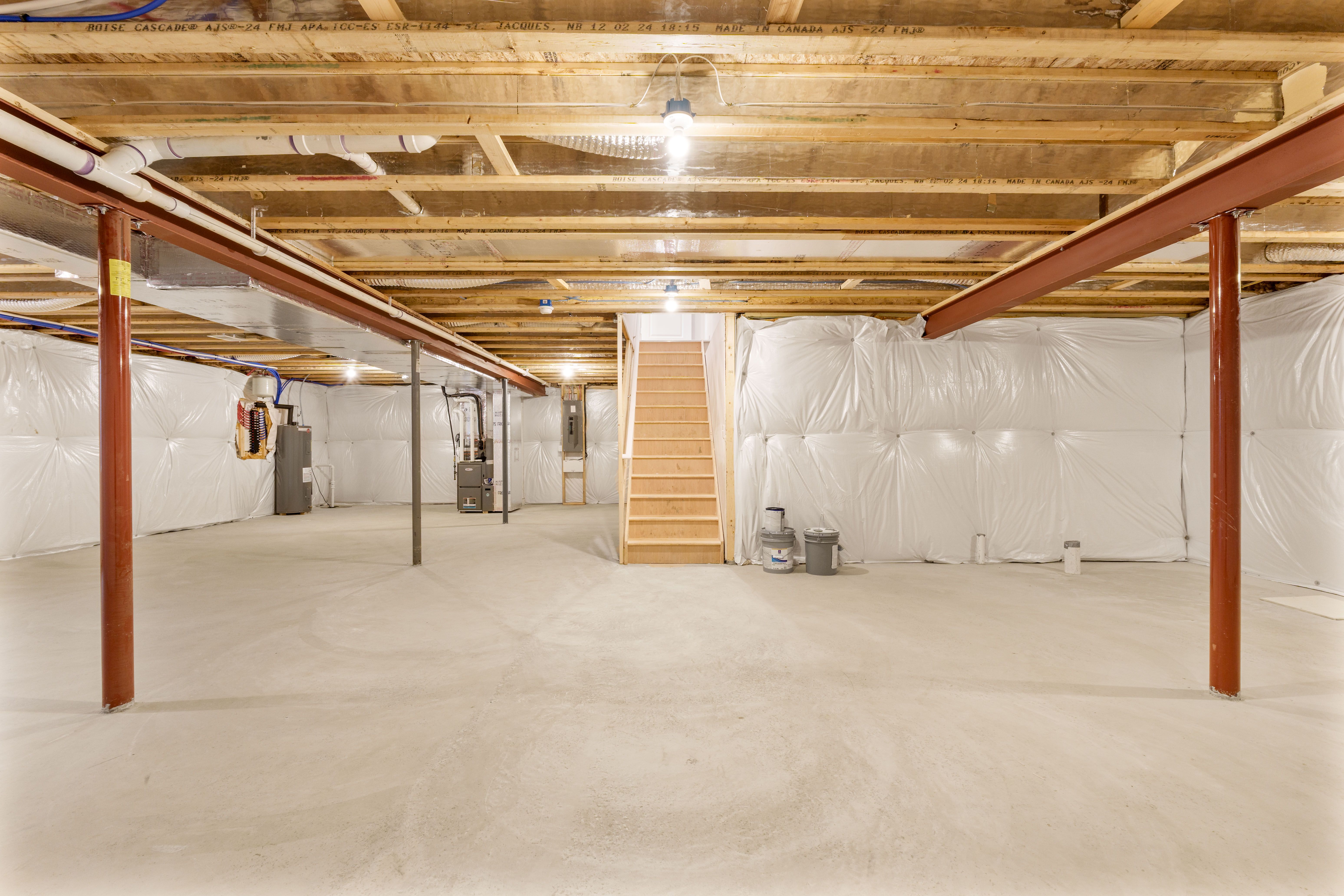 Unfinished basement showing central staircase, mechanical systems, insulated walls, and open floor space
