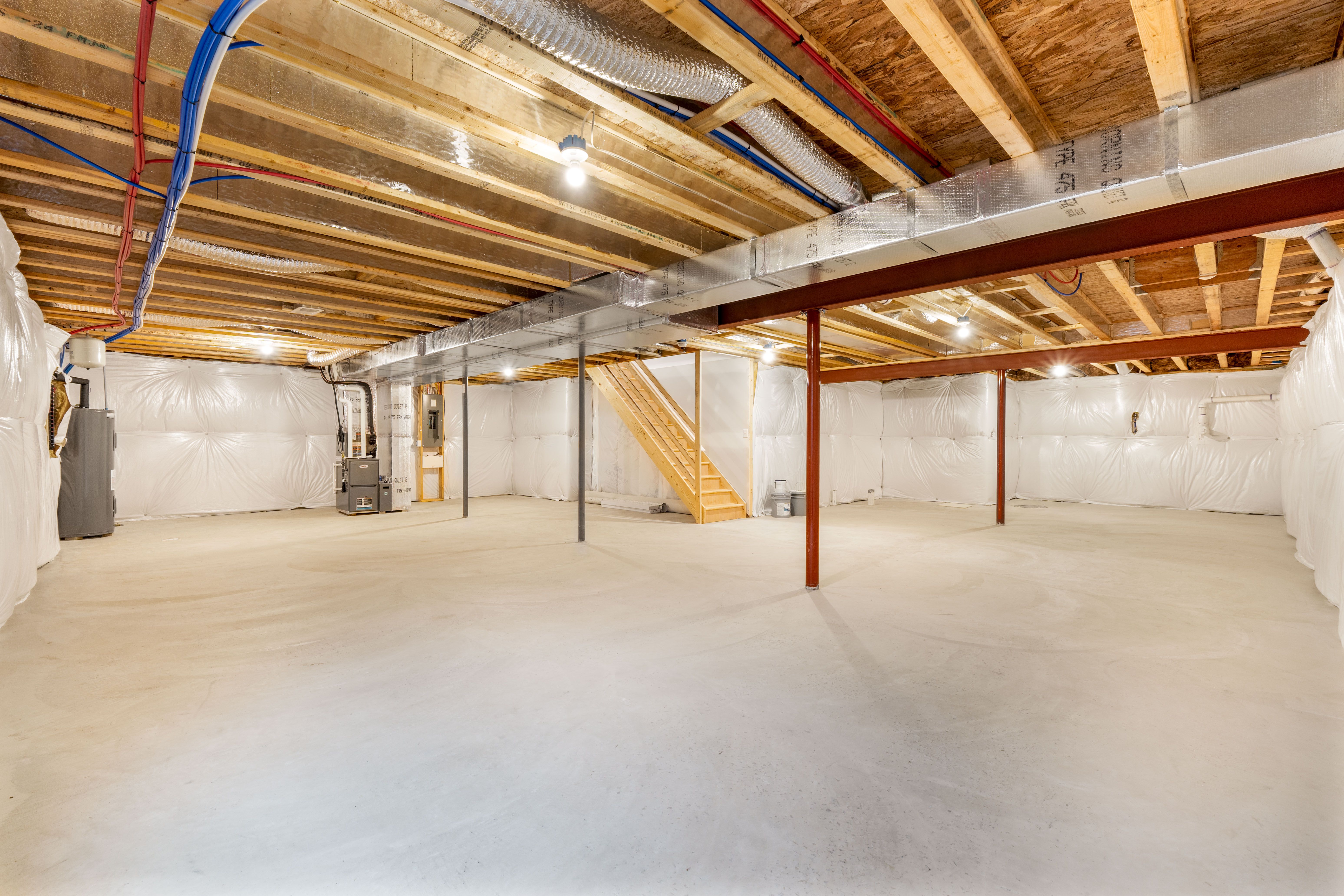 Angled view of unfinished basement with exposed ductwork, steel beams, support columns, and concrete flooring