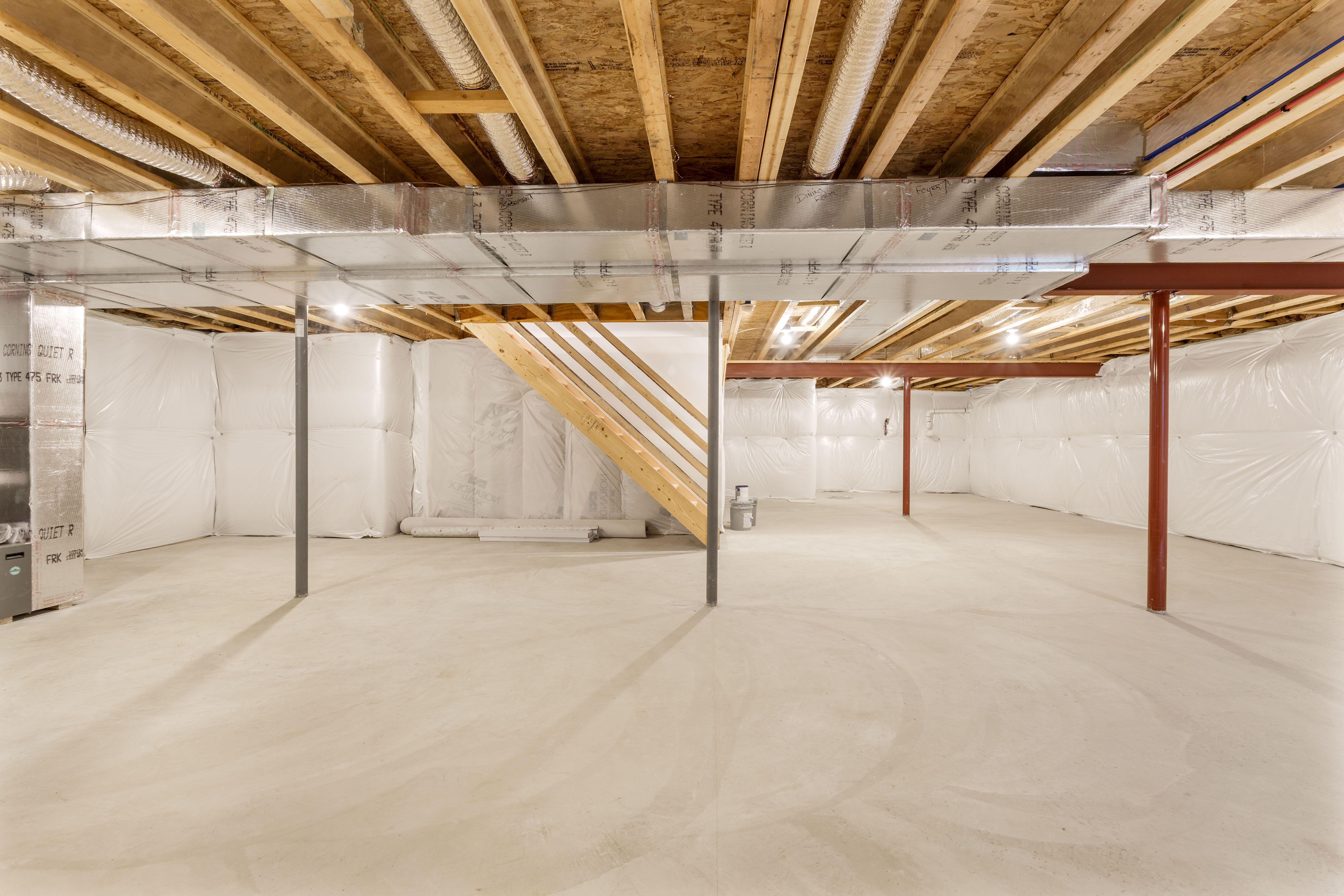 Open unfinished basement area with visible framing, insulation panels, ductwork, and staircase underside