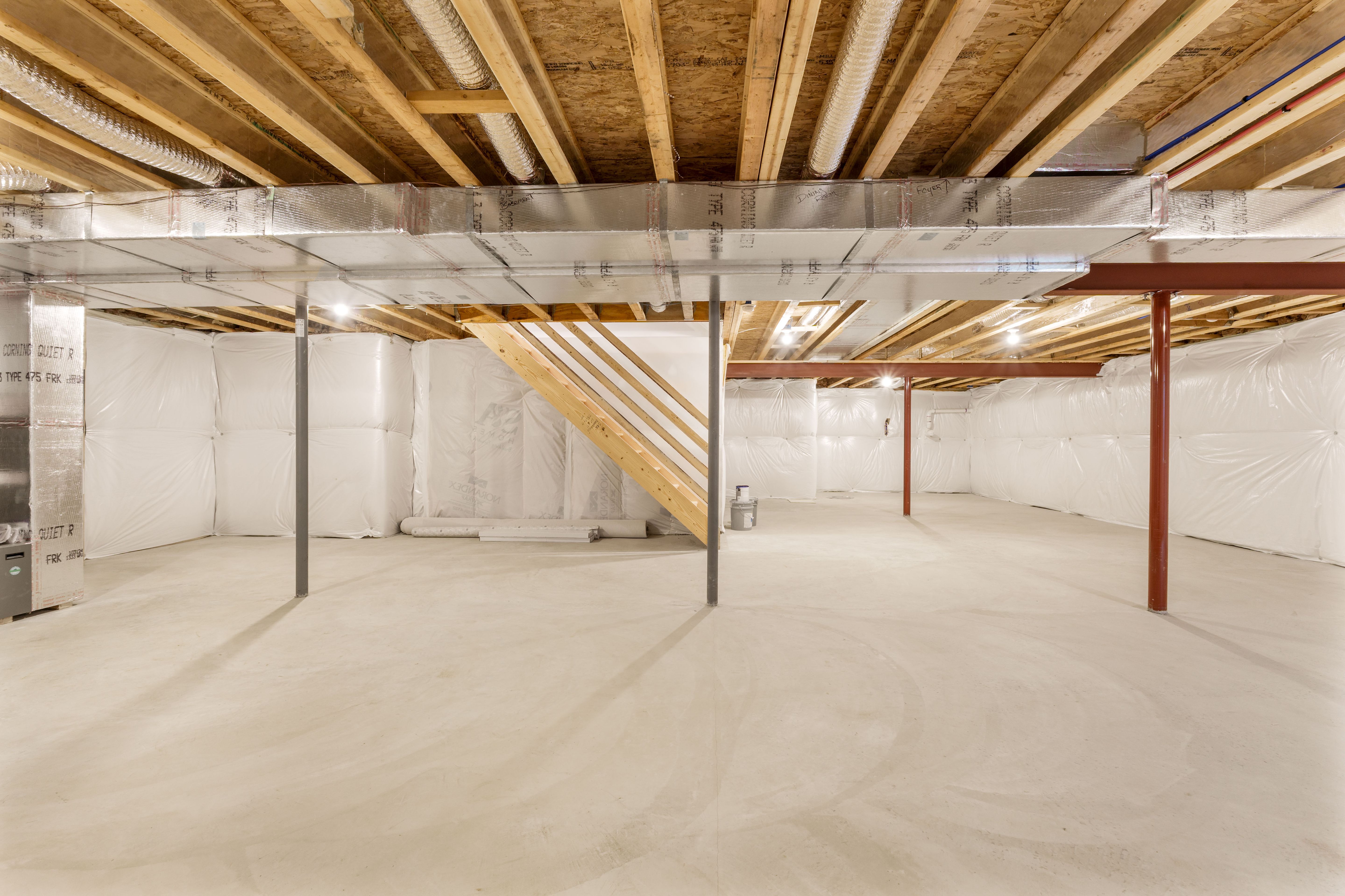 Open unfinished basement area with visible framing, insulation panels, ductwork, and staircase underside