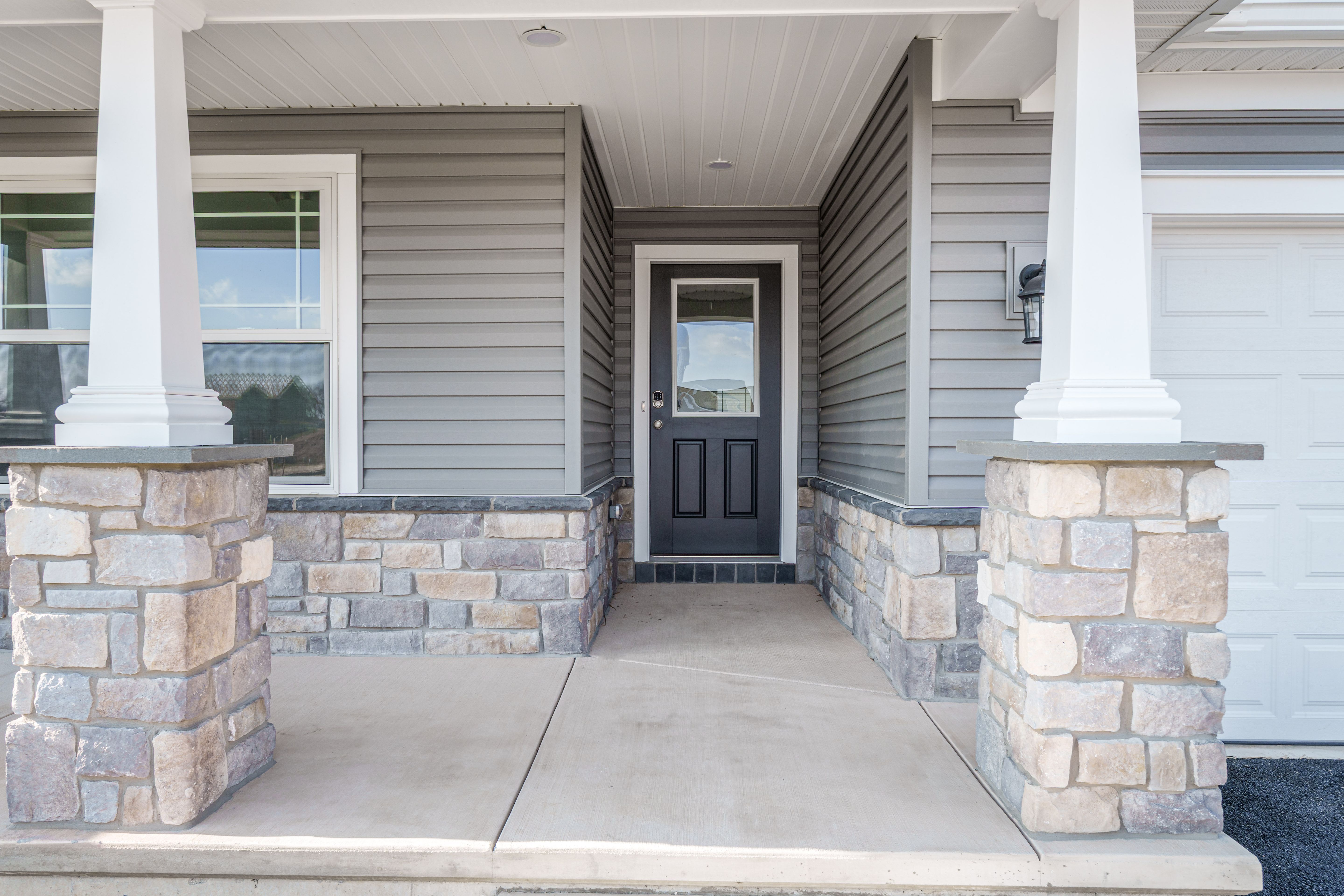 Covered front porch with stone columns, white trim, and dark entry door