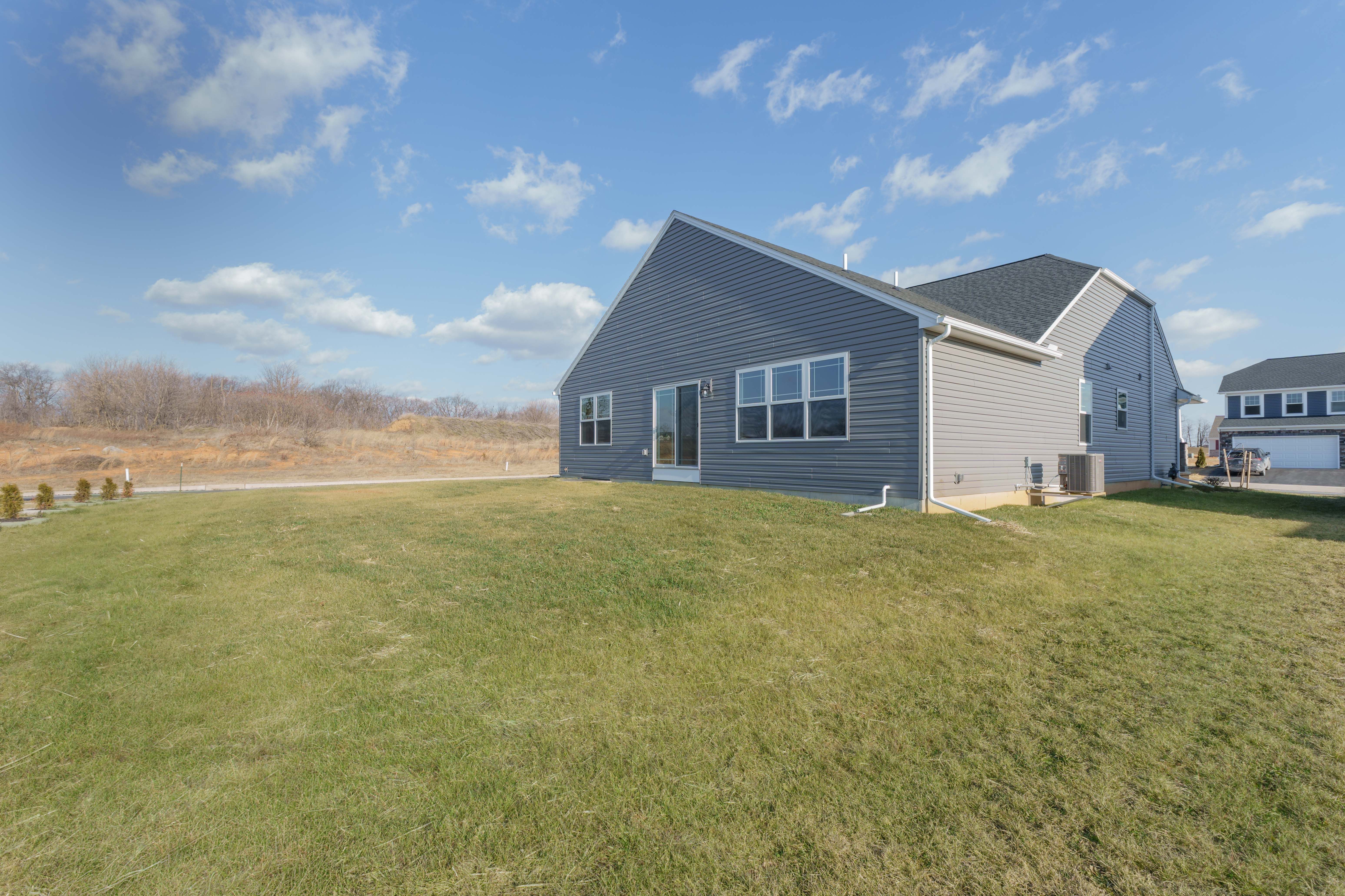 Rear exterior of gray ranch with sliding glass door, backyard, and open views behind home