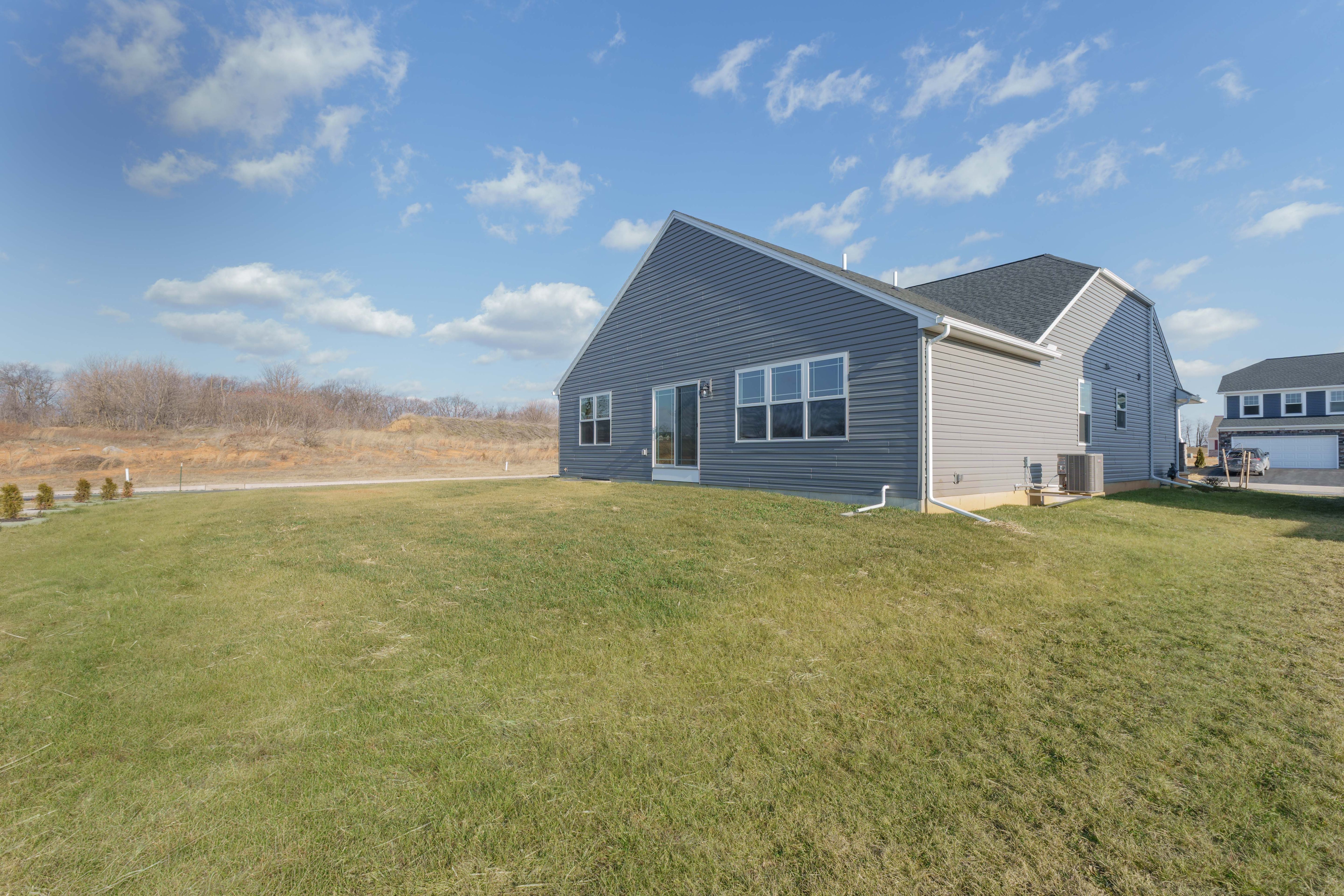 Rear exterior of gray ranch with sliding glass door, backyard, and open views behind home