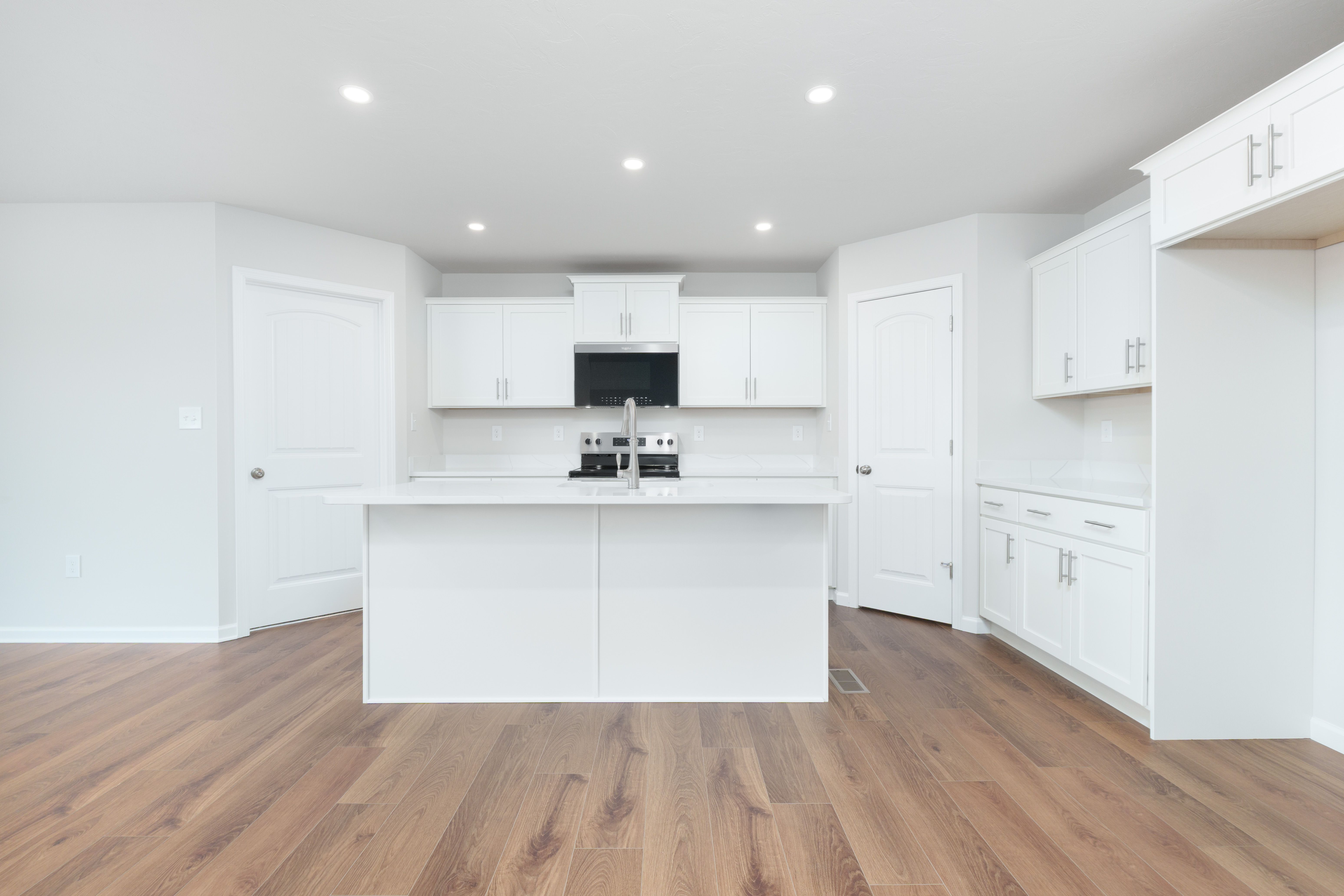 Open kitchen with white cabinets, center island, pantry doors, and luxury vinyl plank flooring