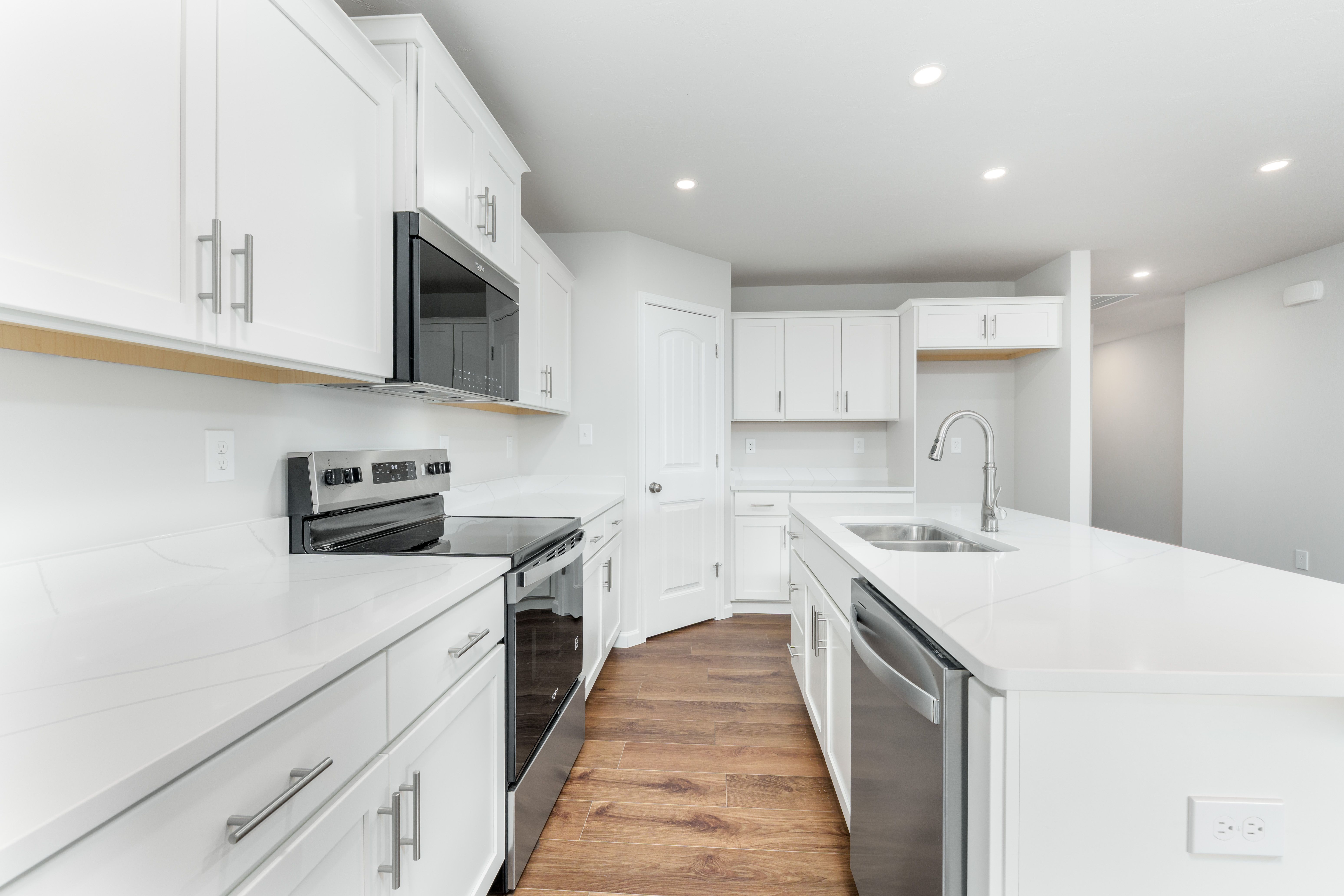 Galley-style kitchen with white cabinets, quartz counters, stainless range, and island with sink