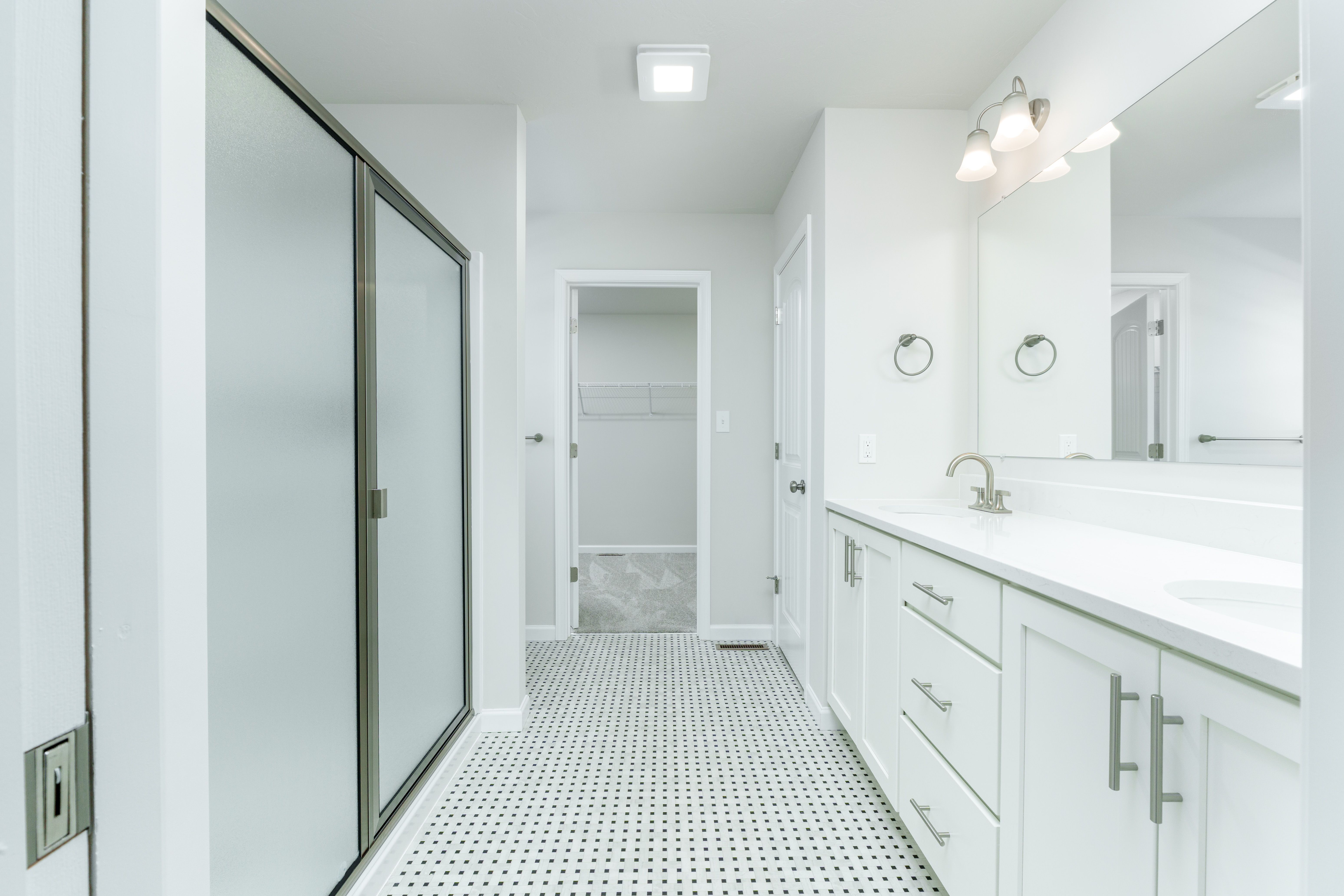 Owners bath with double vanity, framed mirrors, tile flooring, and glass shower enclosure