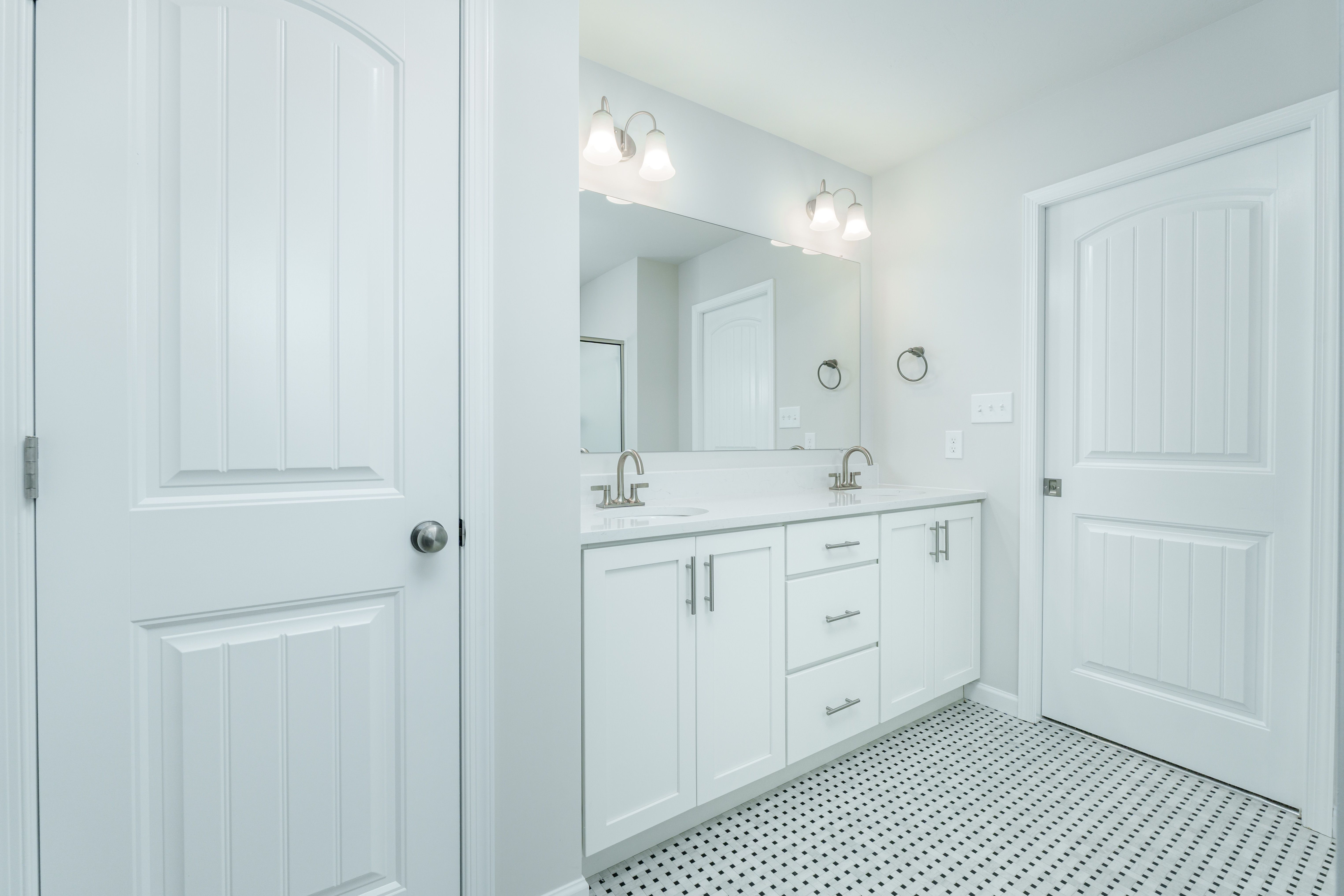 Bright owners bath with glass shower, dual sinks, large mirror, and patterned tile flooring
