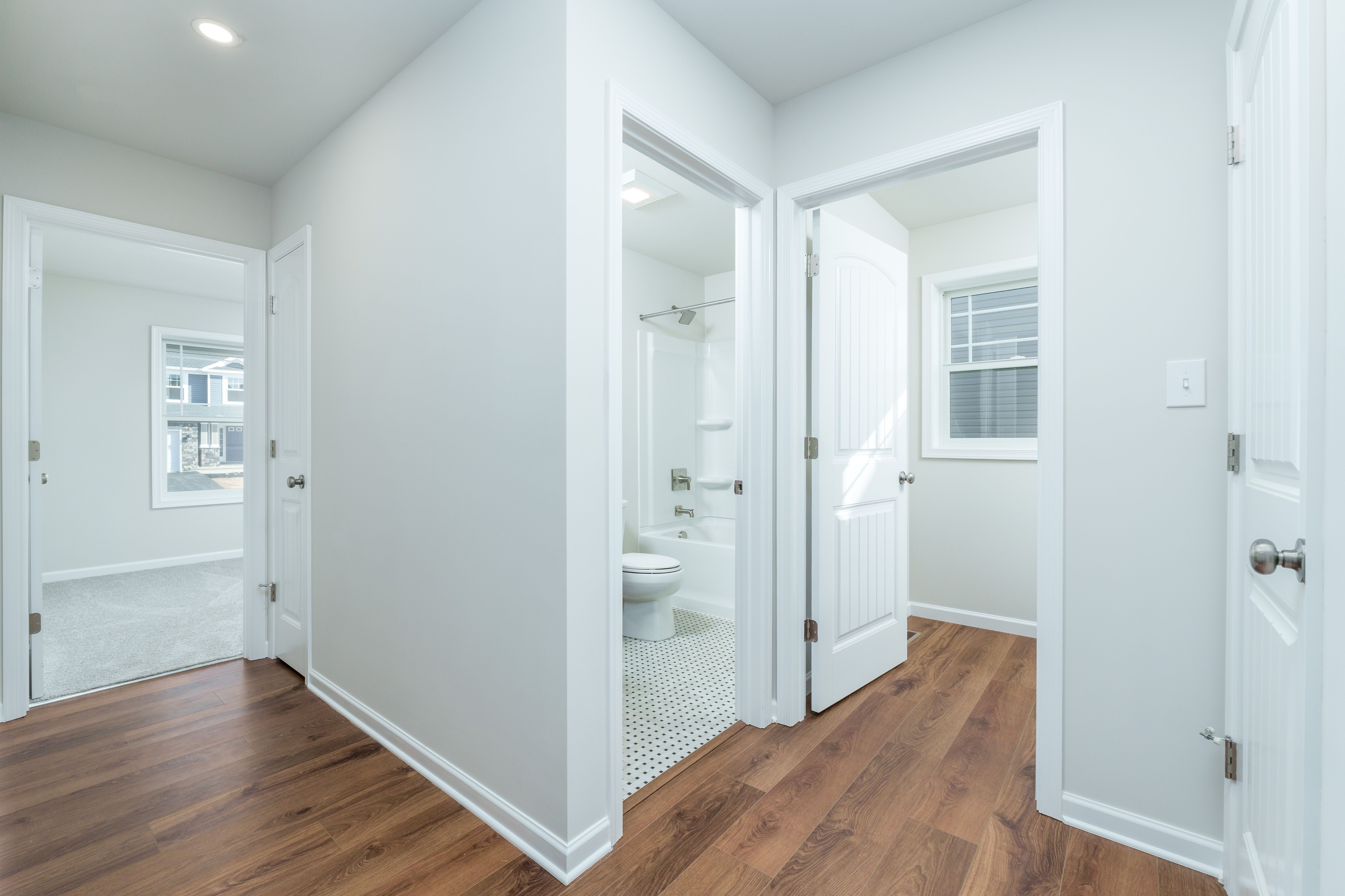 Hallway with multiple doorways, luxury vinyl plank flooring, and view into carpeted bedroom