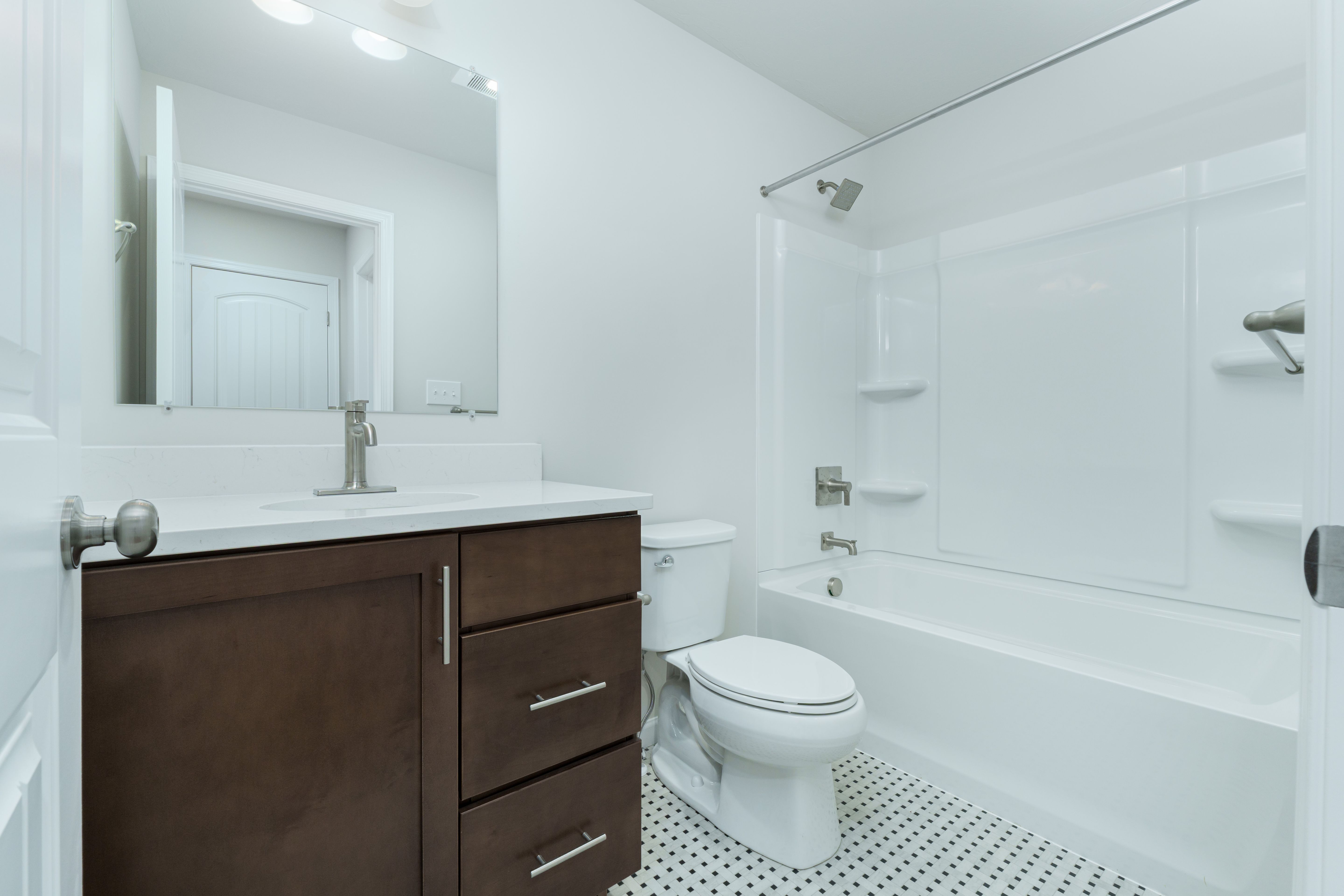 Full bathroom with dark wood vanity, white countertop, tub shower combo, and mosaic tile flooring