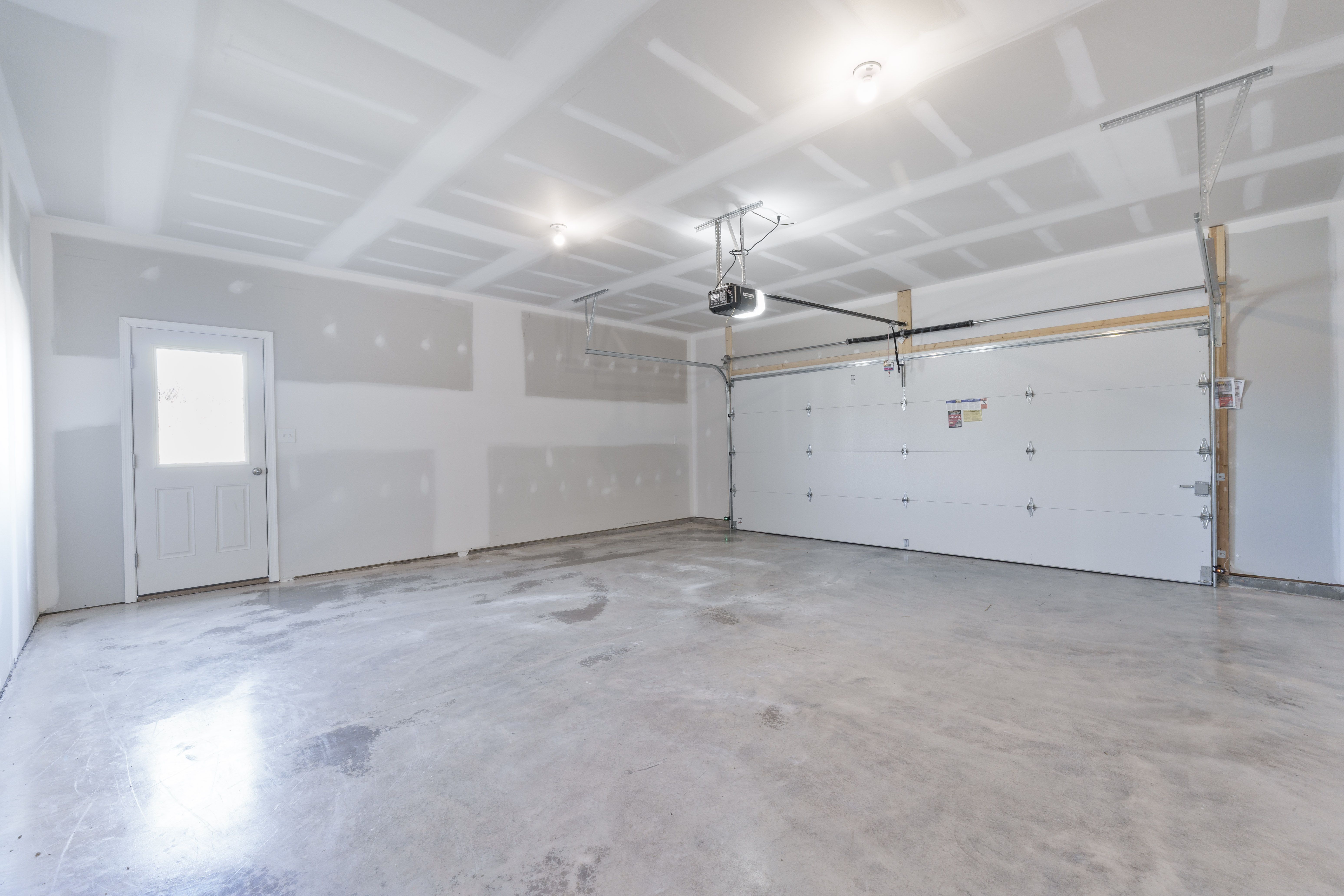 Two-car garage with concrete floor, finished drywall, overhead opener, and service door to exterior