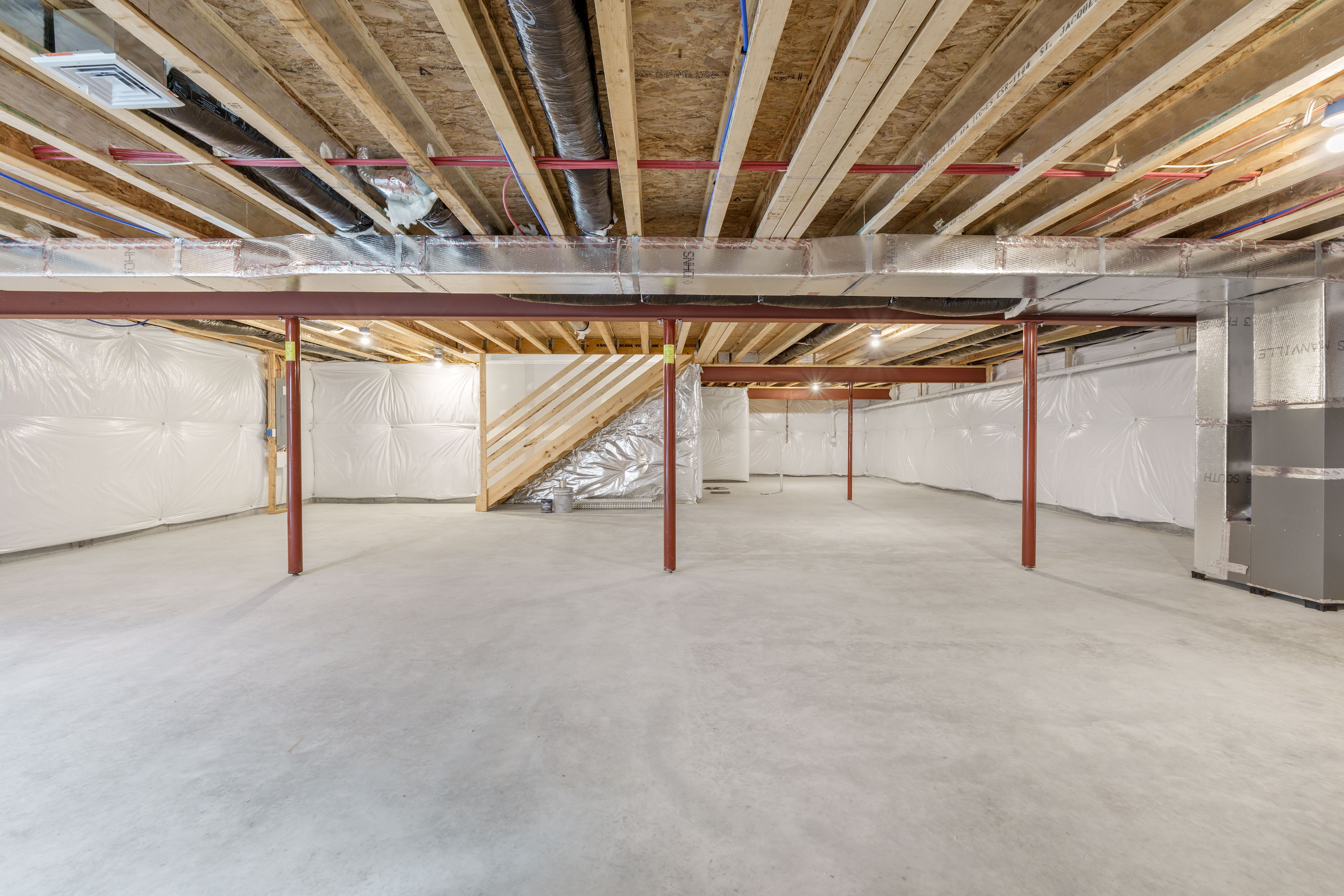 Spacious unfinished basement with support columns, exposed ductwork, and insulated foundation walls