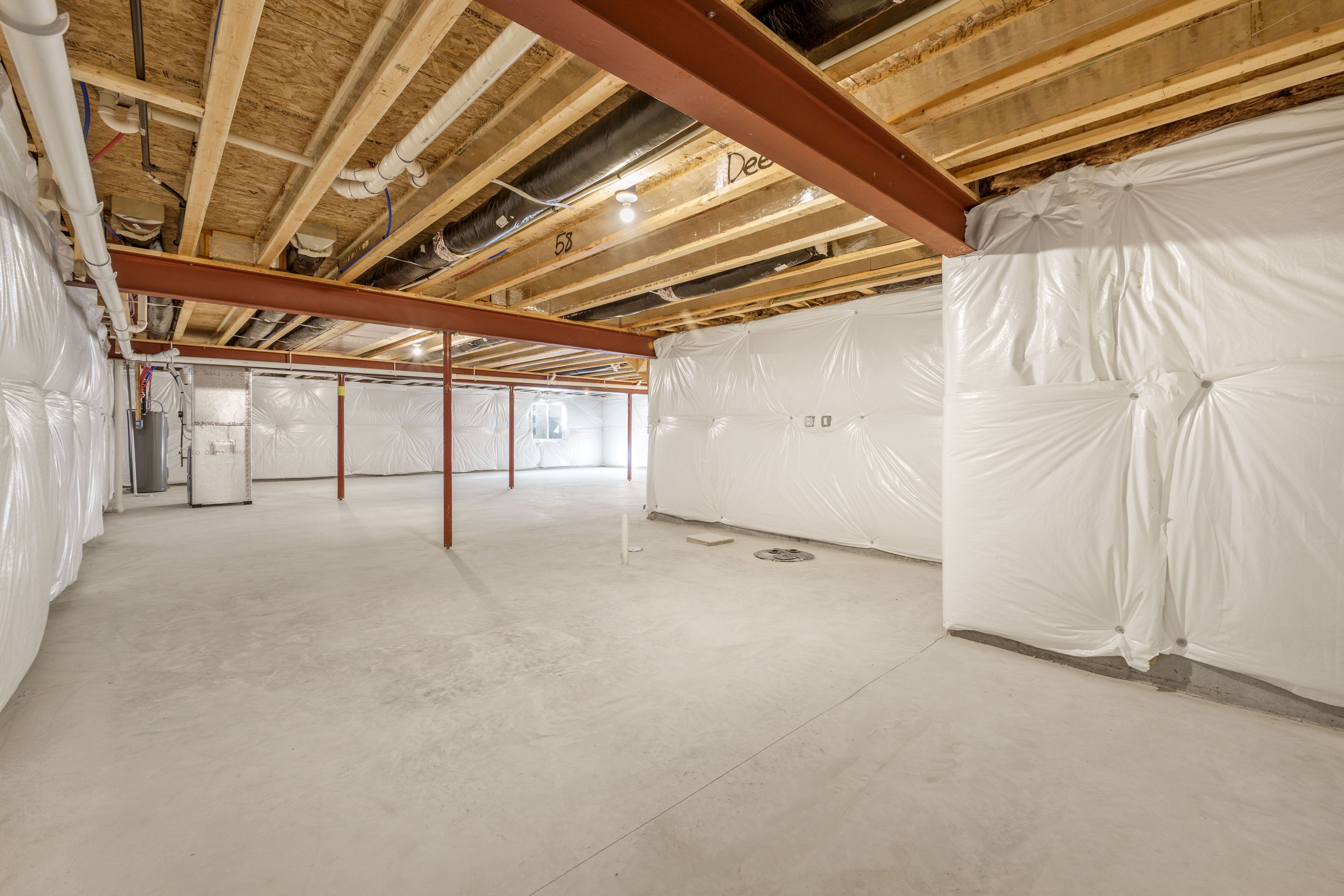 Open unfinished basement with concrete floor, steel beams, utility area, and wrapped insulation walls