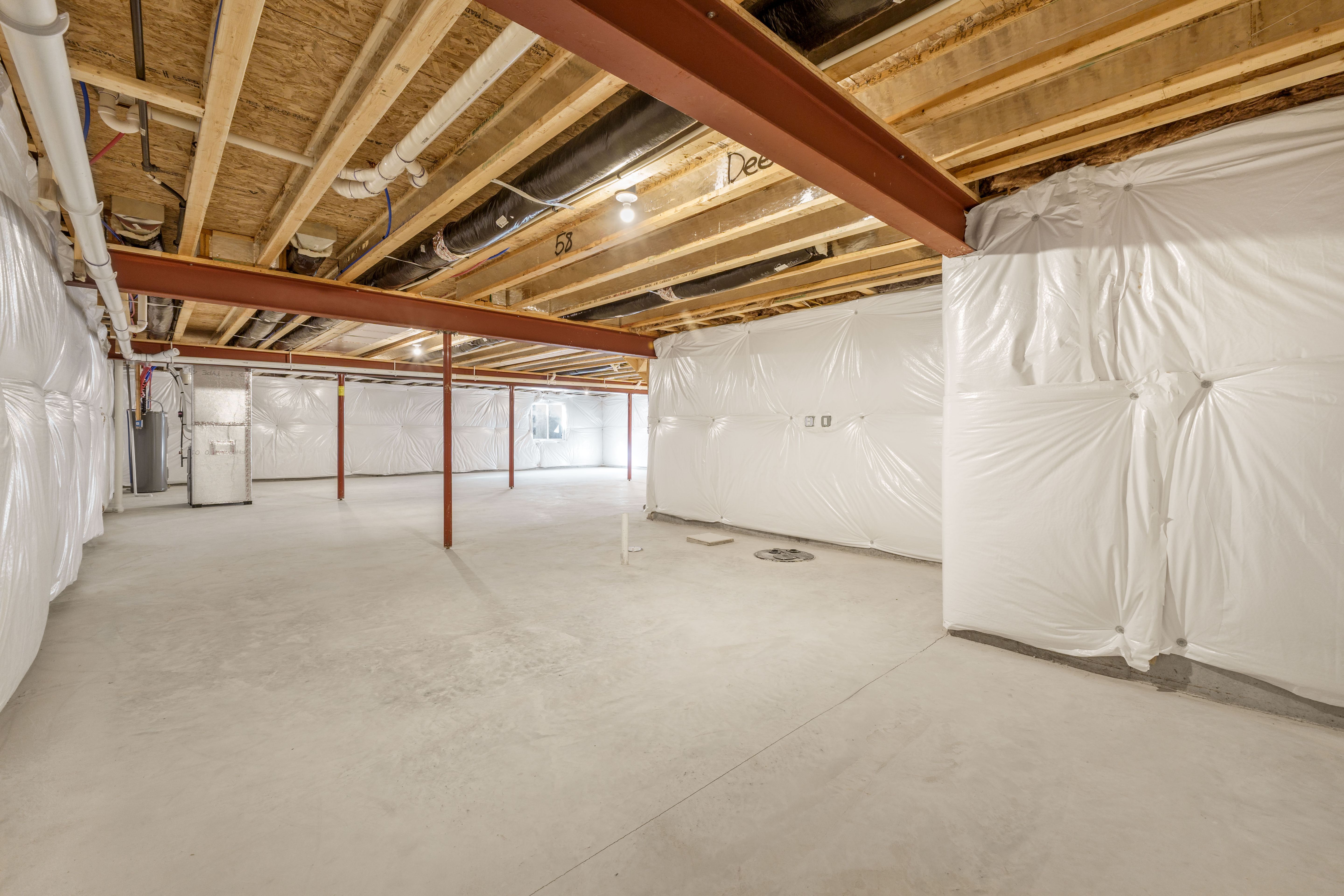 Open unfinished basement with concrete floor, steel beams, utility area, and wrapped insulation walls