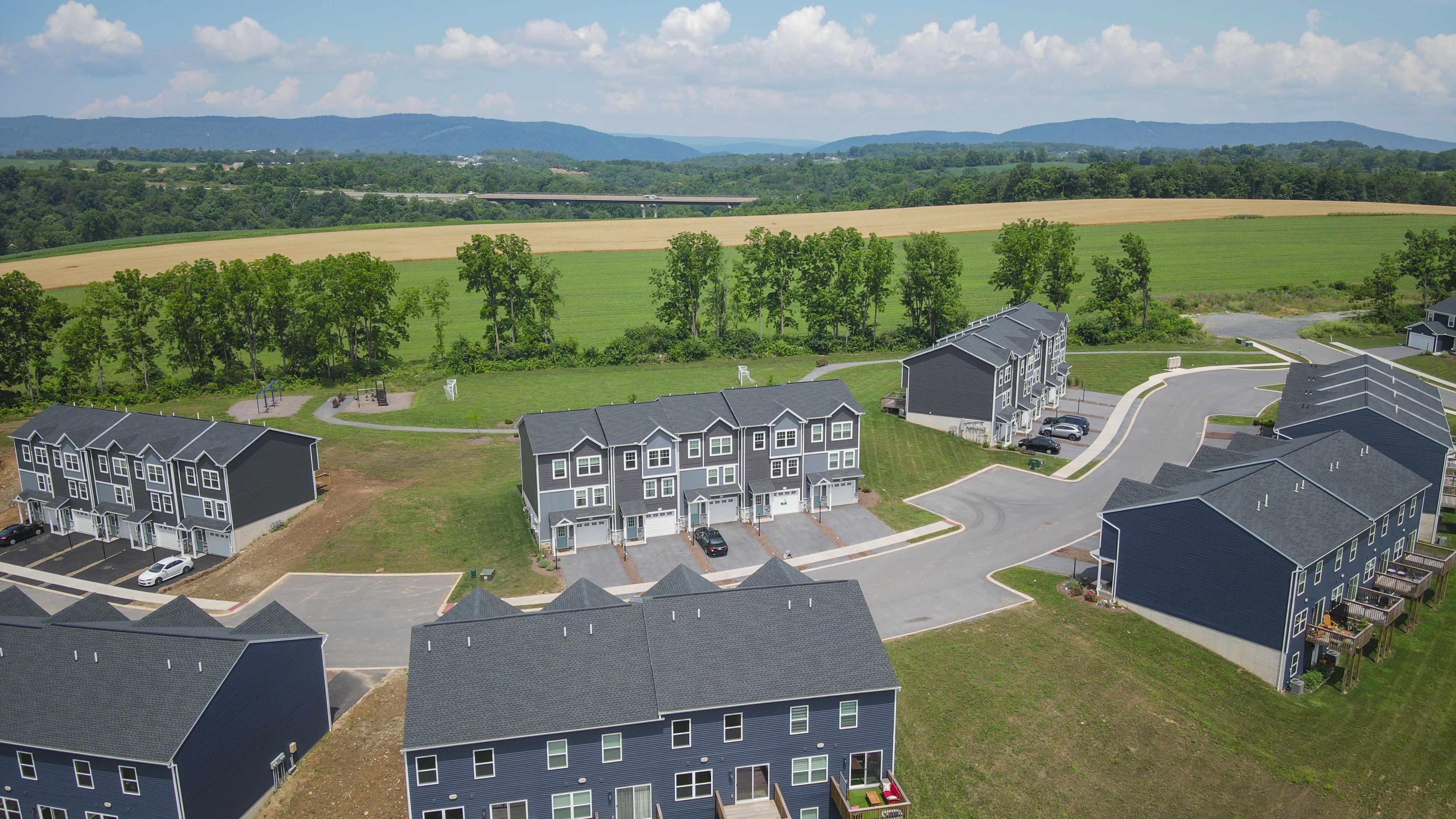 Aerial view of townhome community with garages, sidewalks, open green space, playground, and mountain backdrop