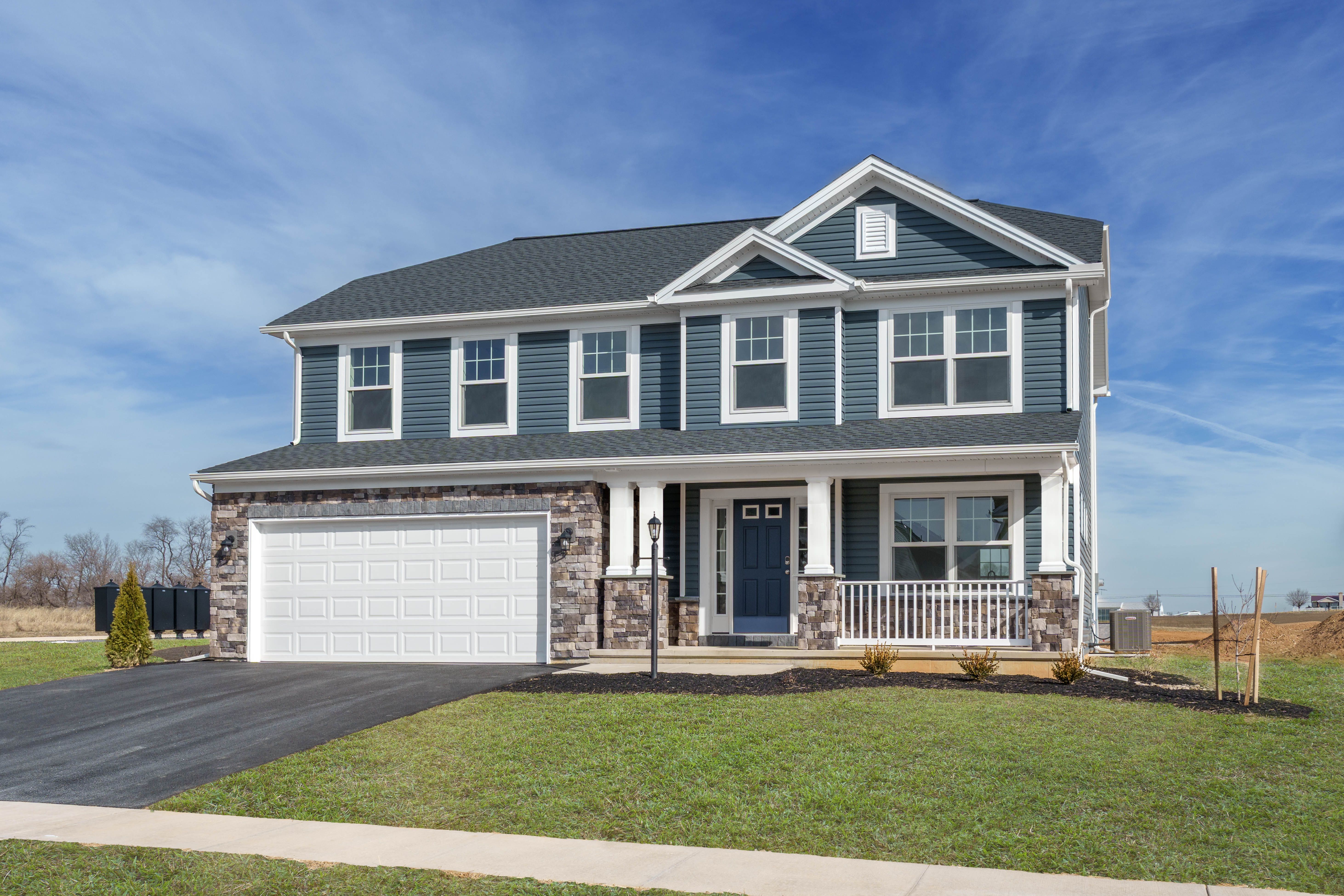 Two-story blue home with stone accents, white trim, covered front porch, and two-car garage