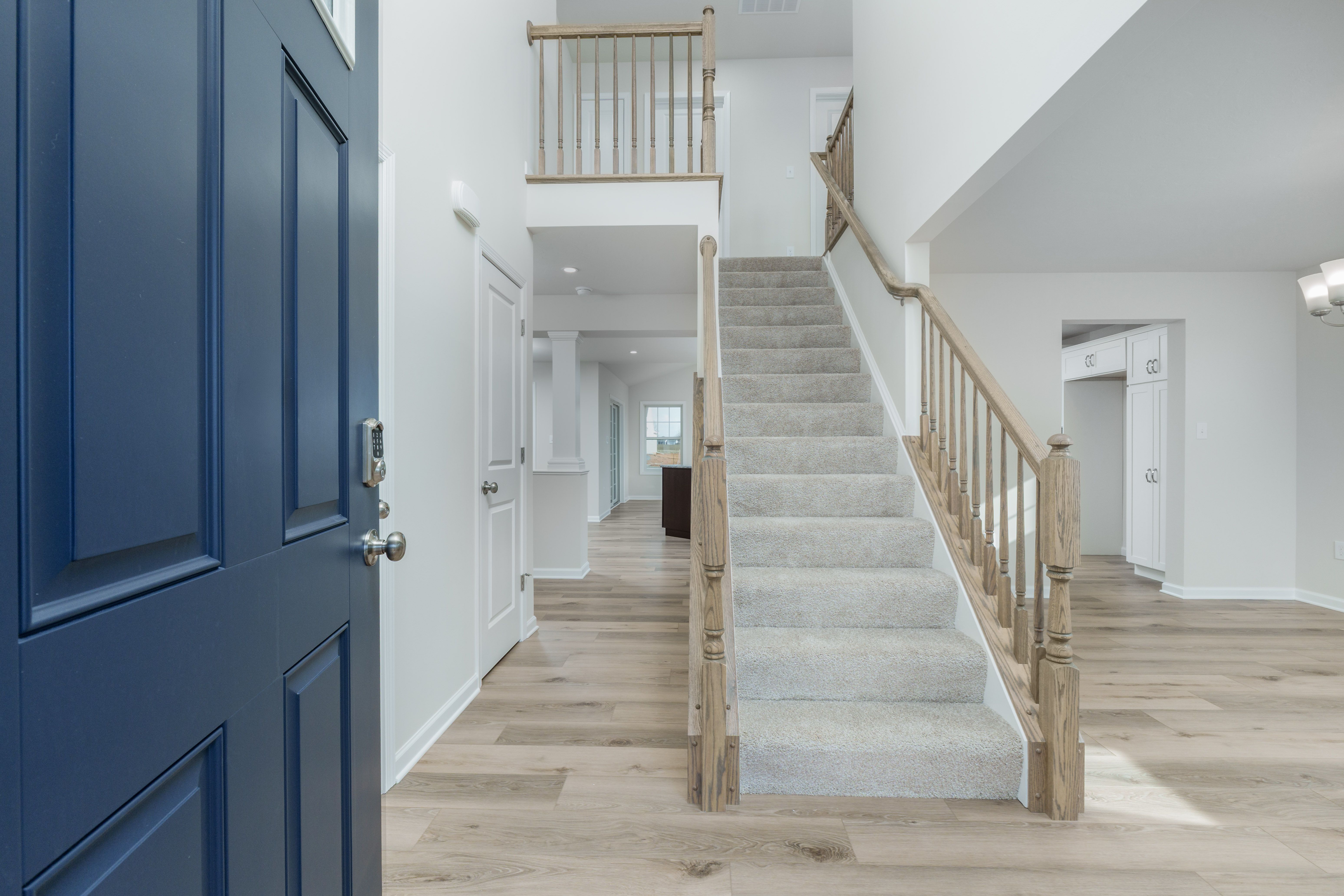Foyer with blue front door, carpeted staircase, wood railing, and luxury vinyl plank flooring.
