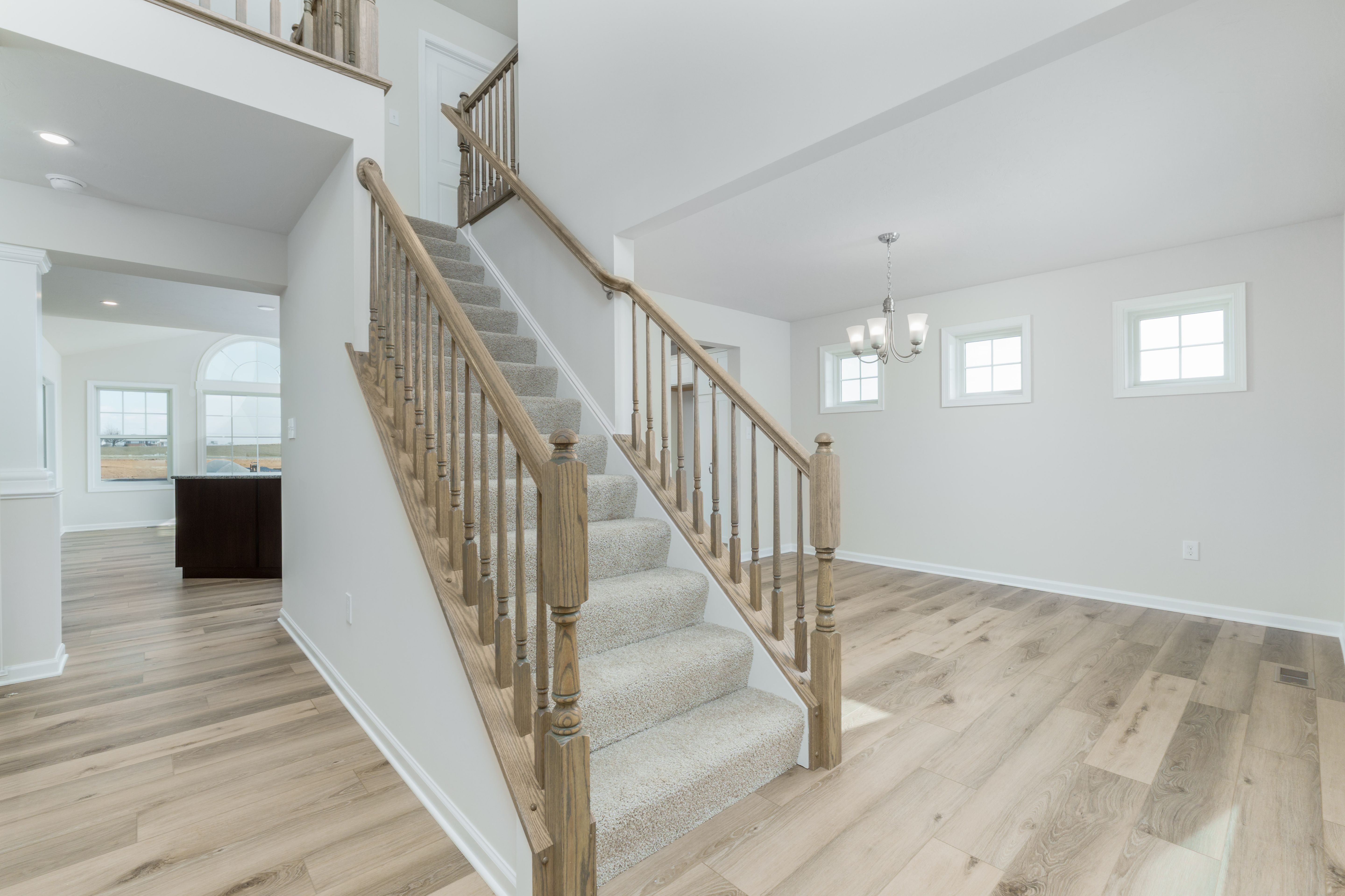 Bright foyer with wood staircase, open railing, and luxury vinyl plank flooring throughout main level.