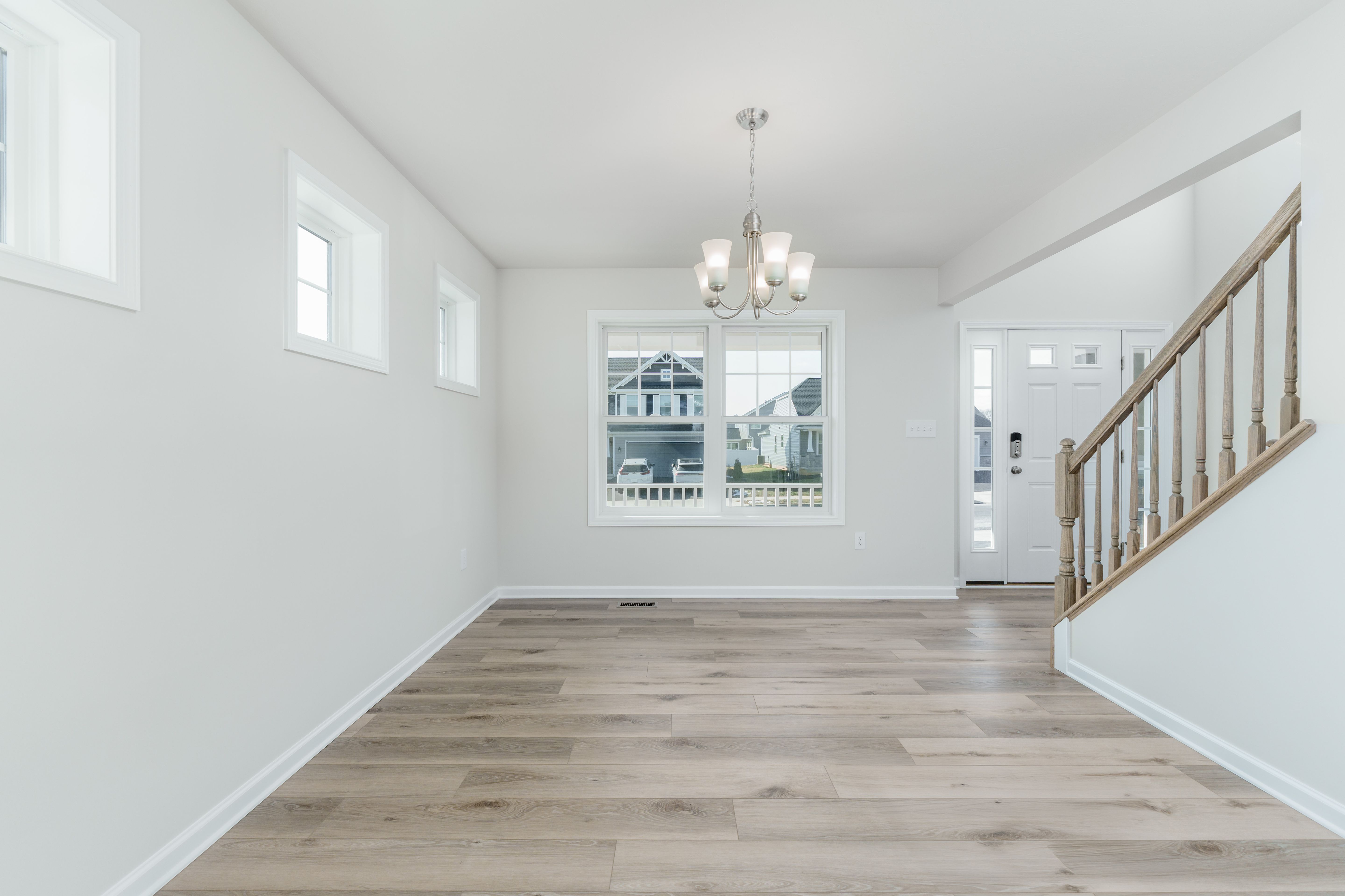 Dining area with luxury vinyl plank flooring, chandelier, large front window, and staircase with wood railing.