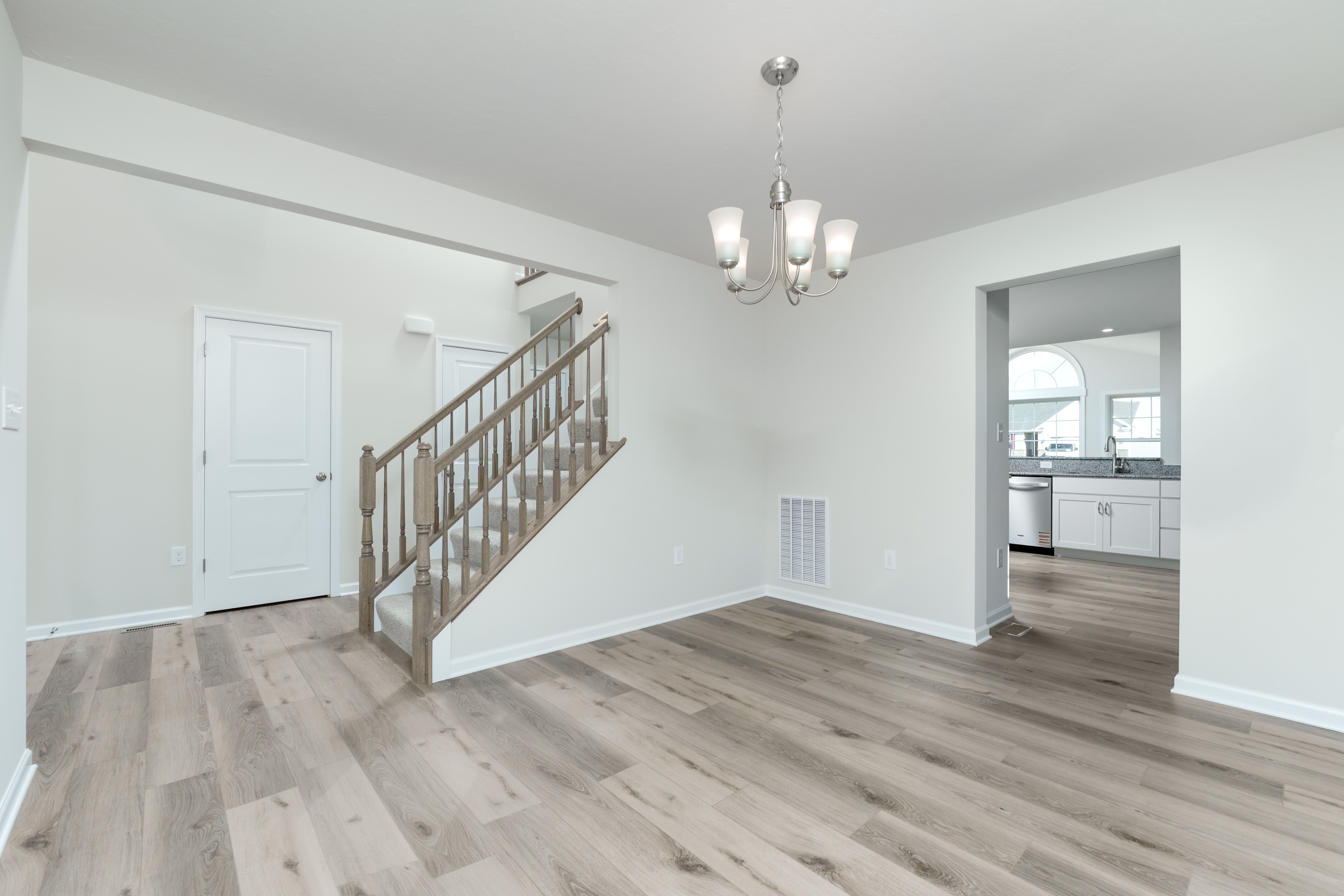 Dining room with chandelier lighting, luxury vinyl plank flooring, and open view to kitchen and stairs.