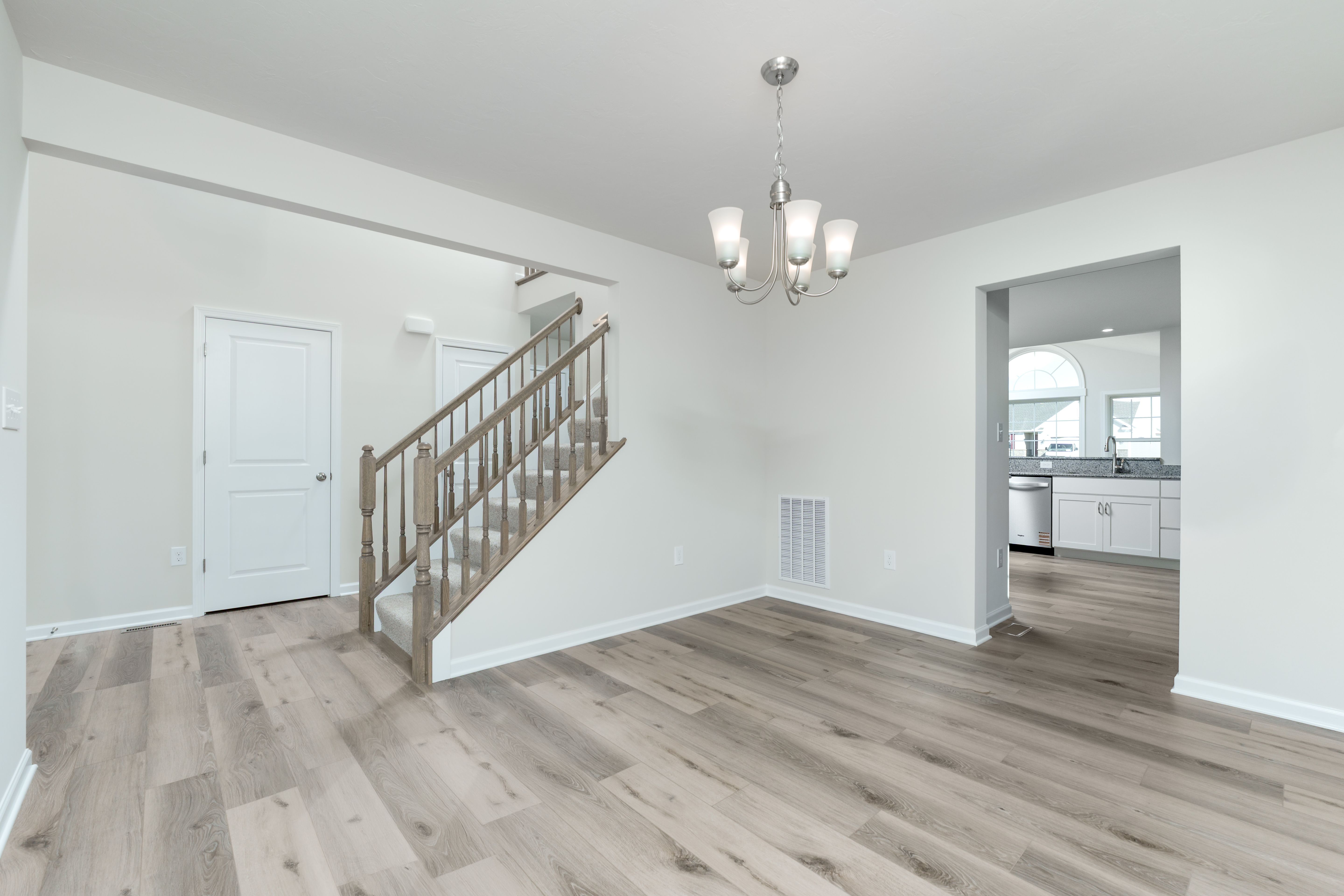 Dining room with chandelier lighting, luxury vinyl plank flooring, and open view to kitchen and stairs.