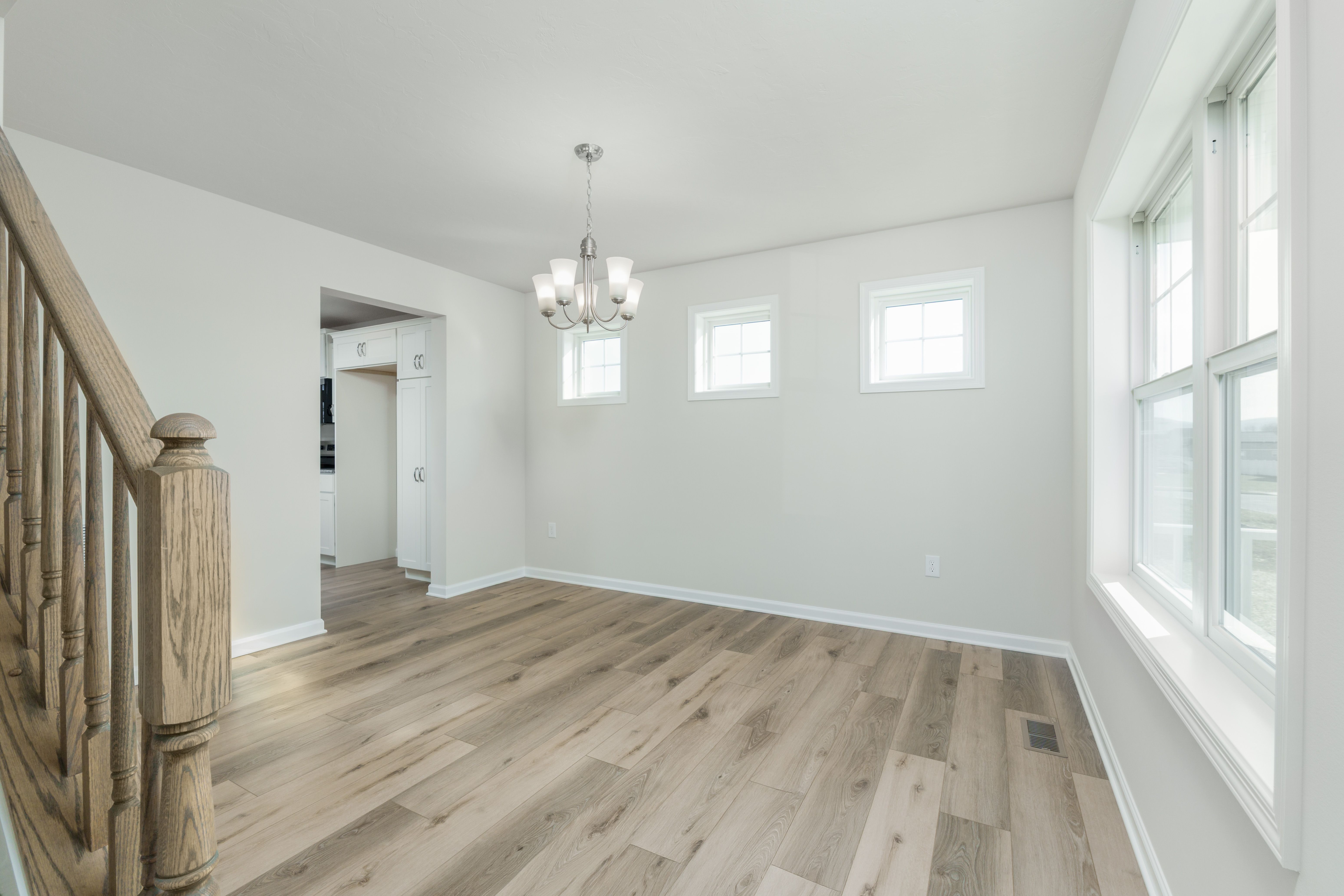Bright dining space with two high windows, large side window, chandelier, and luxury vinyl plank flooring.