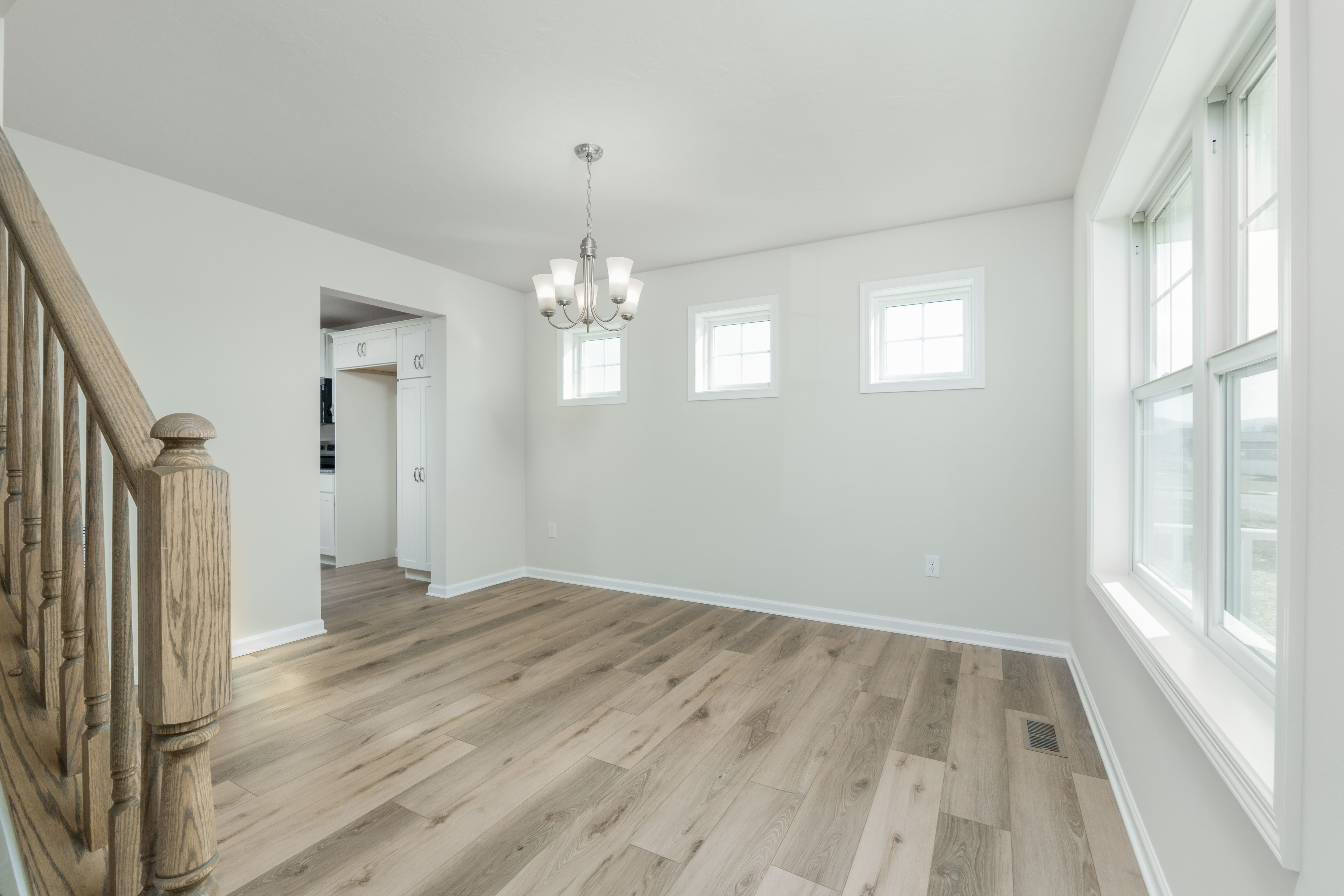 Bright dining space with two high windows, large side window, chandelier, and luxury vinyl plank flooring.