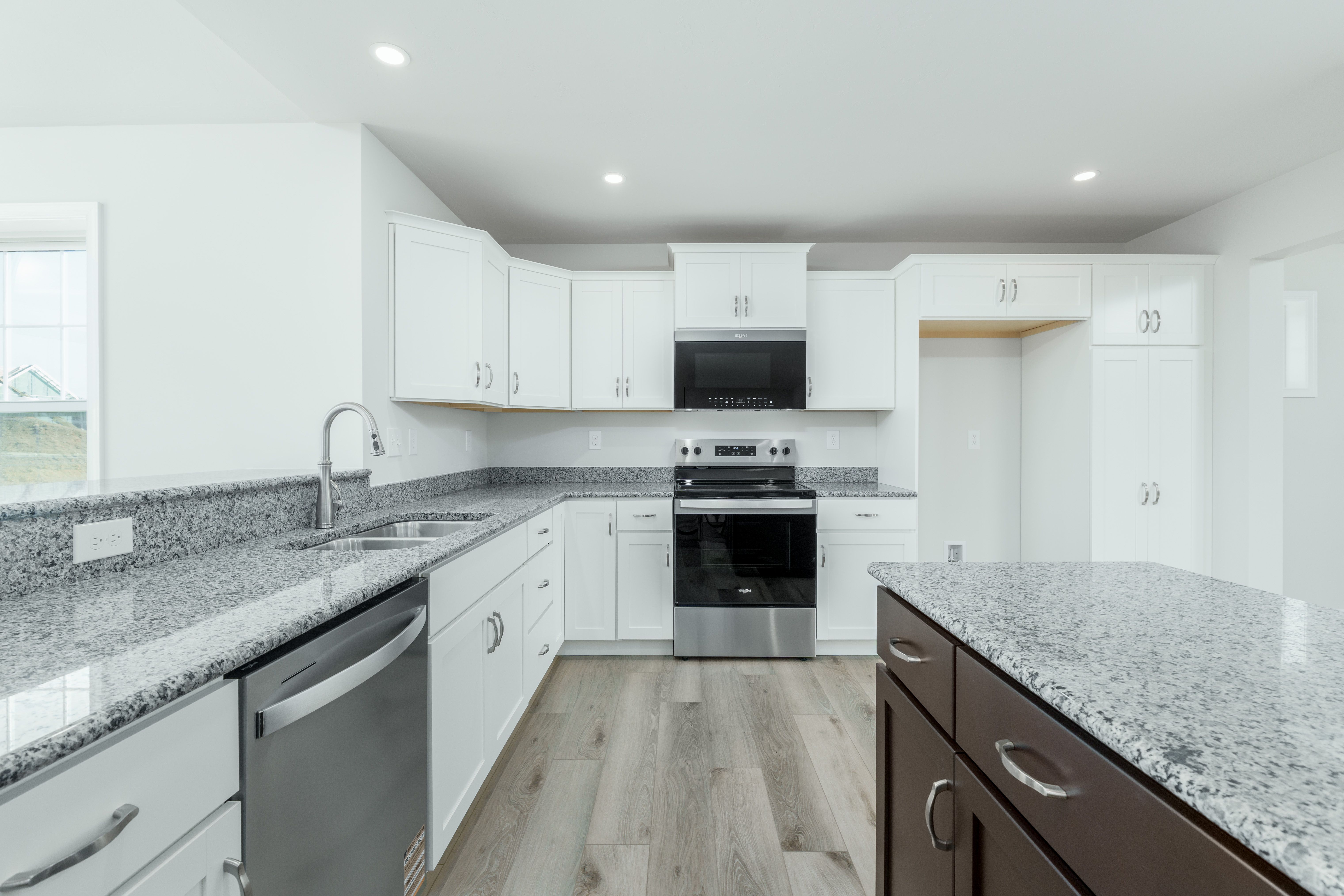 Kitchen with large island, white cabinets, granite countertops, stainless steel appliances, and luxury vinyl plank flooring.