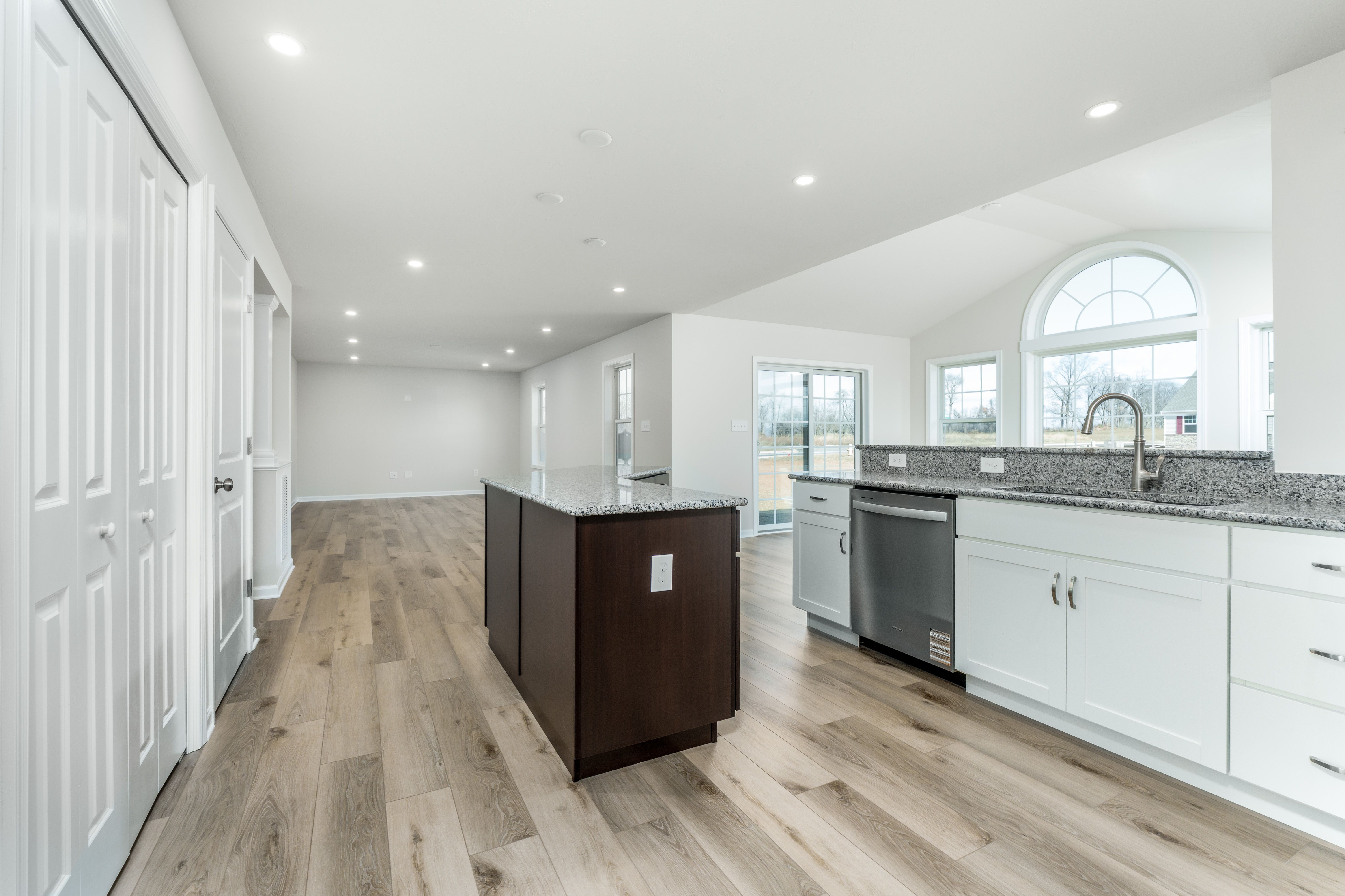 Open kitchen with dark wood island, granite countertops, recessed lighting, and view into bright morning room.