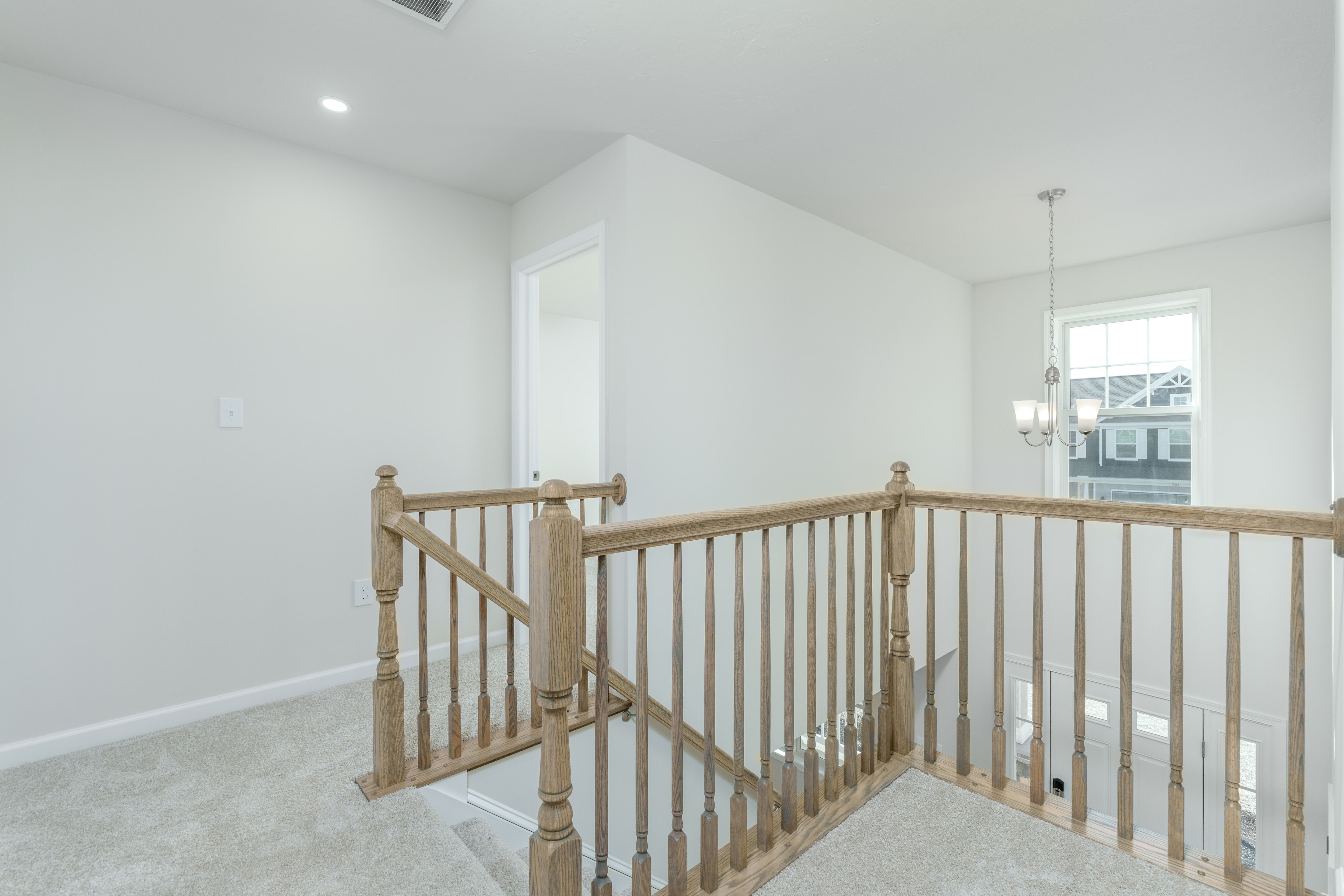 Upper hall with carpet flooring, wood stair railing, window, and hanging light fixture.