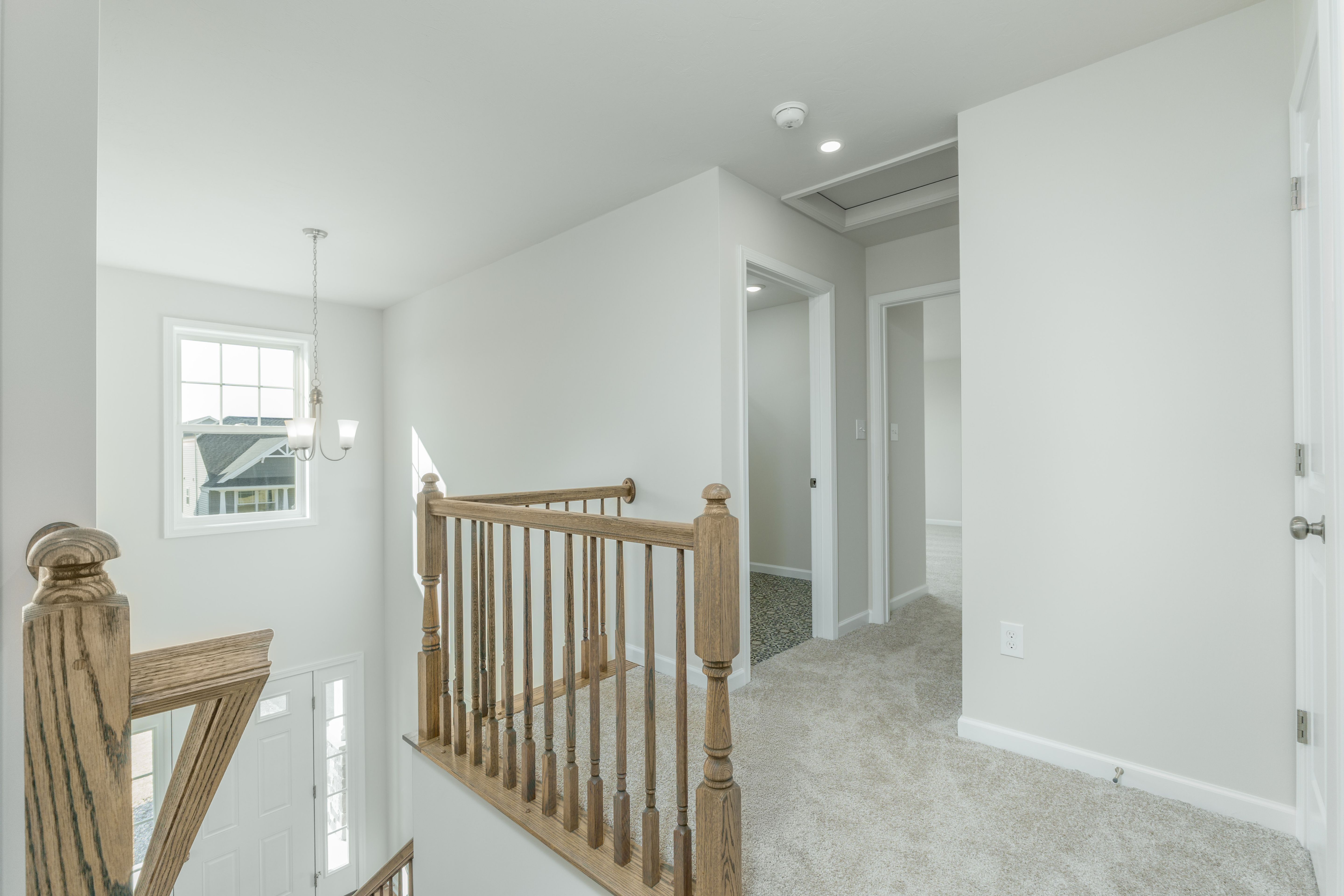 Bright upper hallway with wood balusters, carpeted floors, and open view to staircase below.
